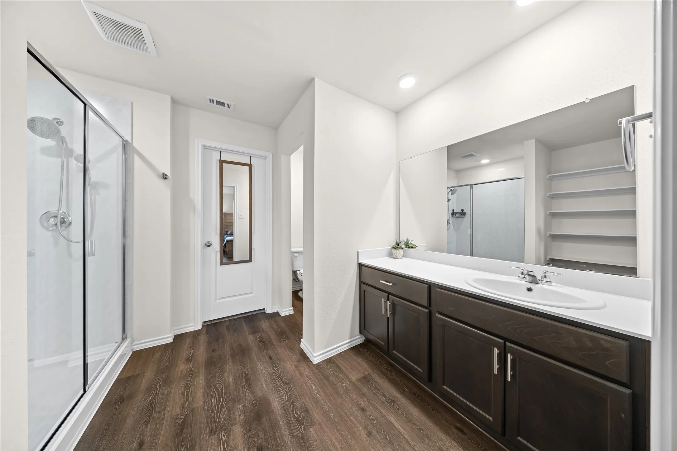 Spacious bathroom featuring a glass-enclosed shower, expansive vanity with a single basin sink, rich wood-finish cabinetry, and wood-finish flooring