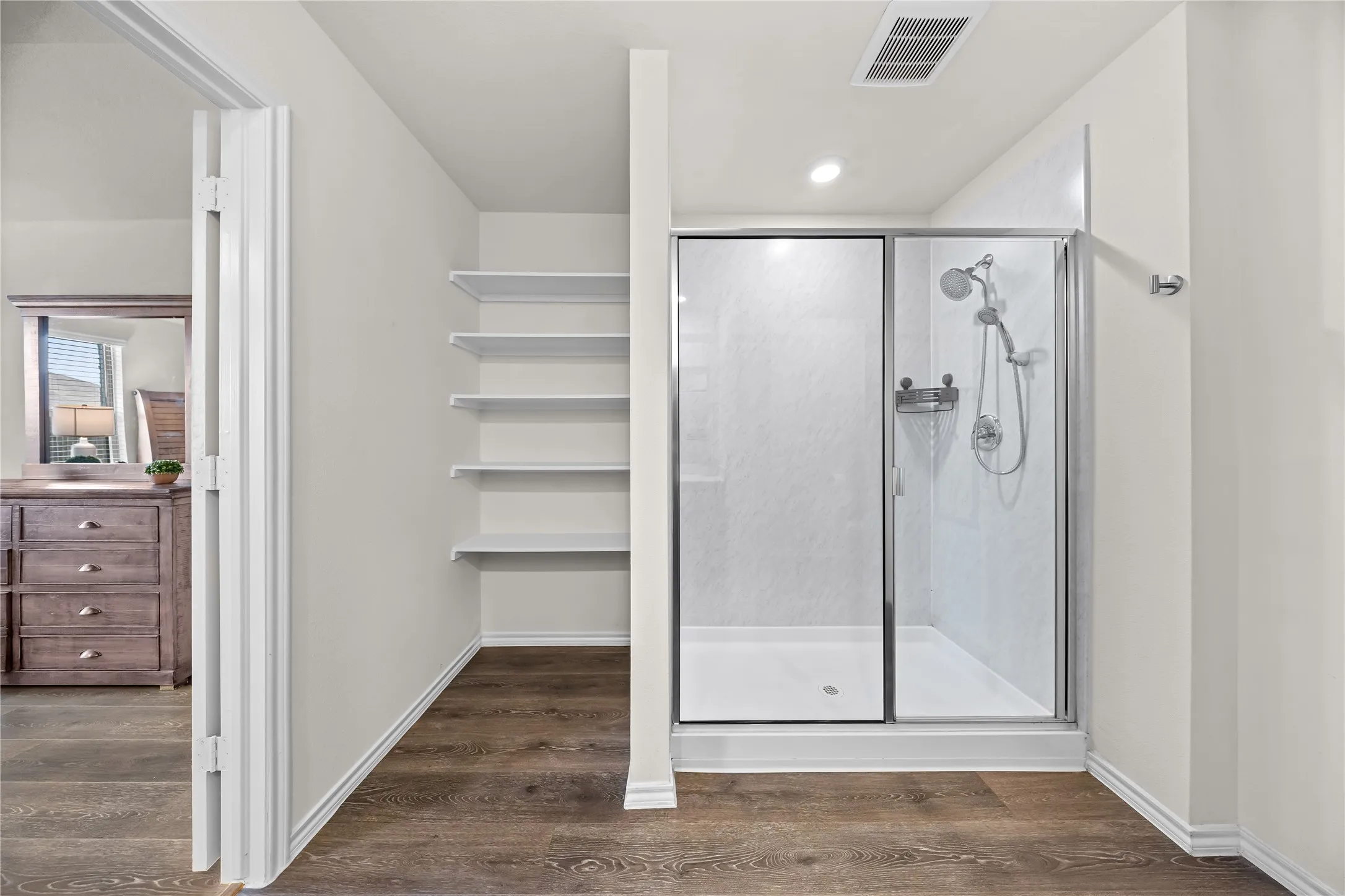 Modern shower enclosure with a glass door, white shower base, and integrated shelving