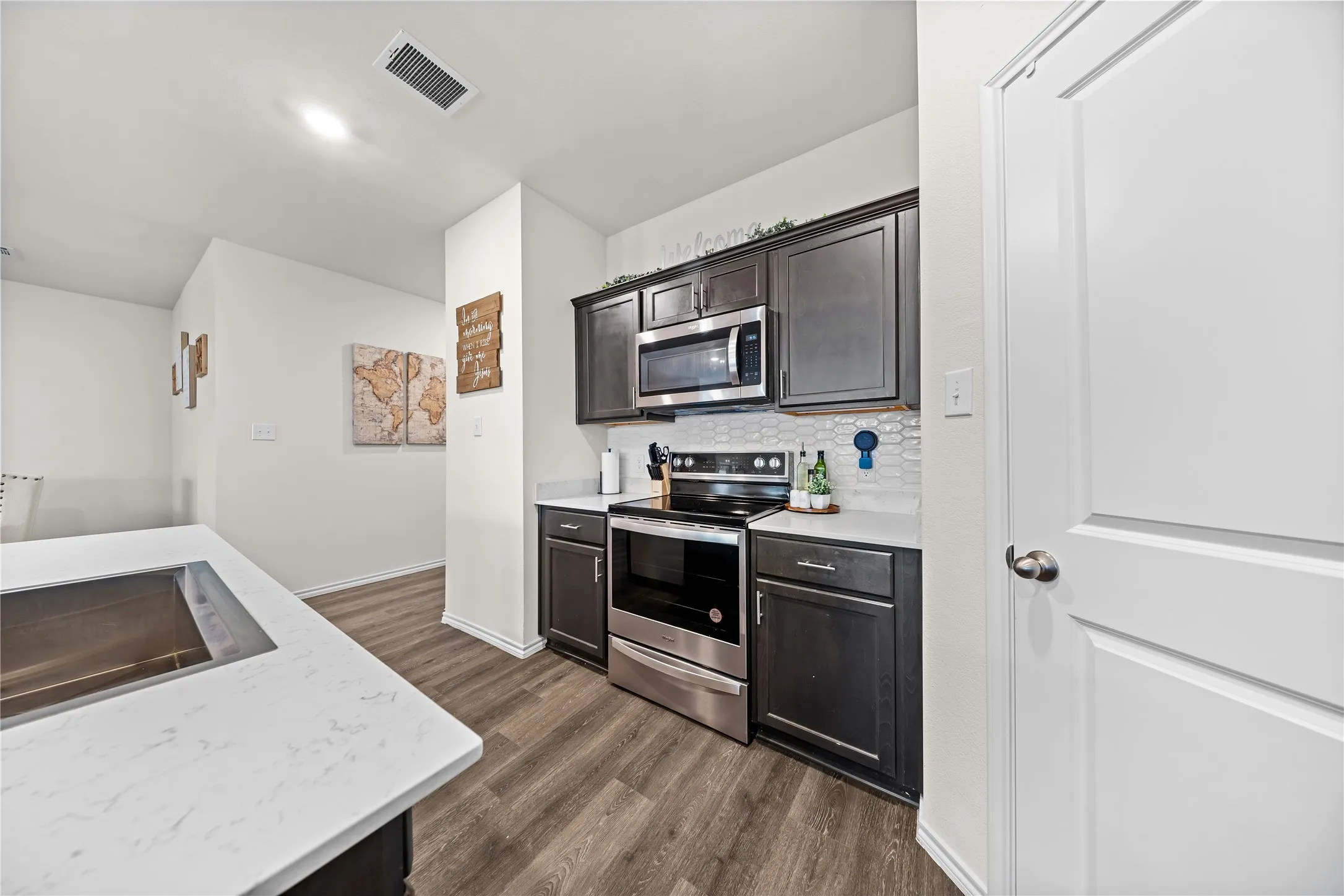 Kitchen featuring dark wood-finish cabinetry, stainless steel appliances including a microwave and range, light-toned countertops, and a white hexagonal tile backsplash