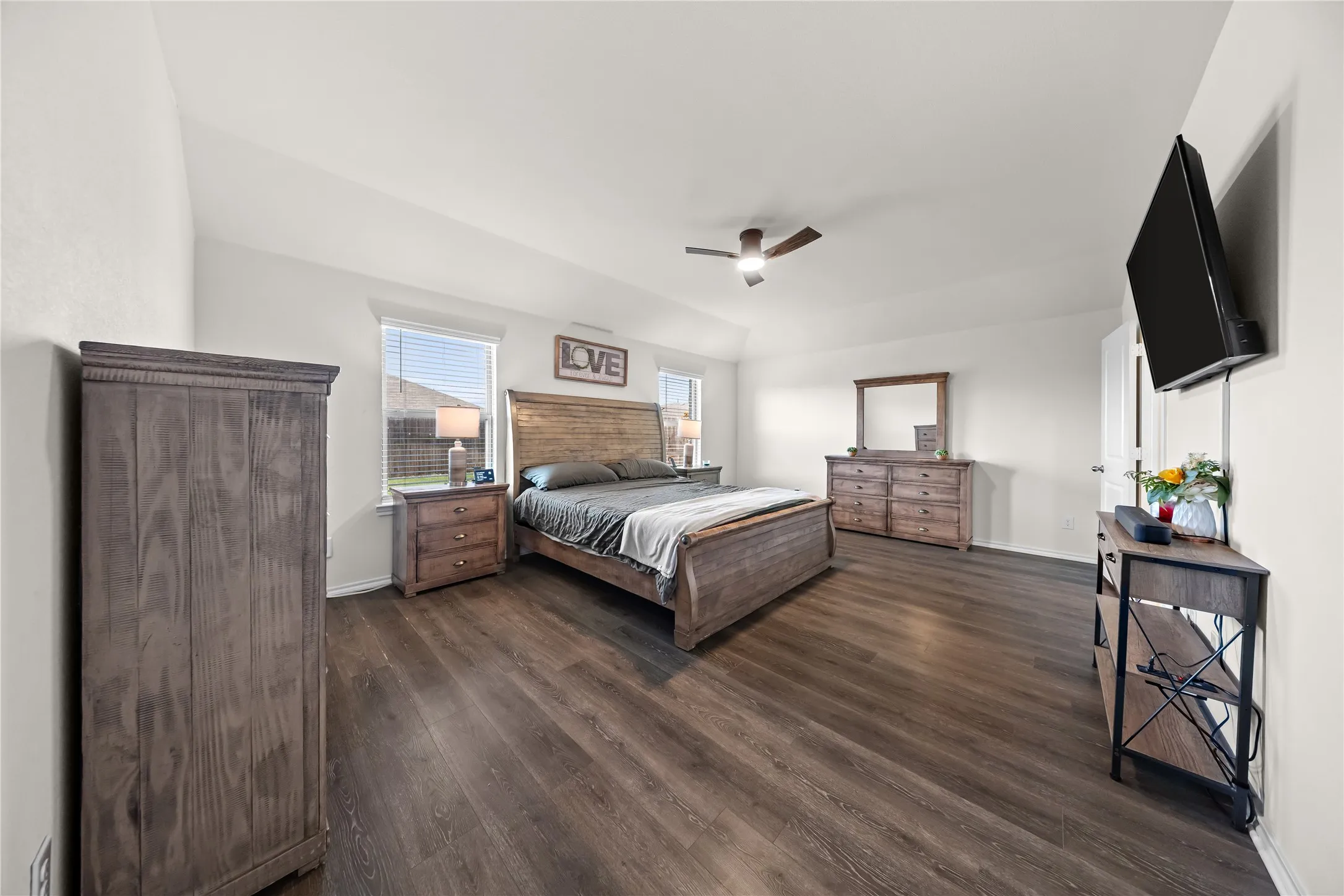 Spacious room featuring wood-finish flooring, two windows with blinds, a ceiling fan, and white walls