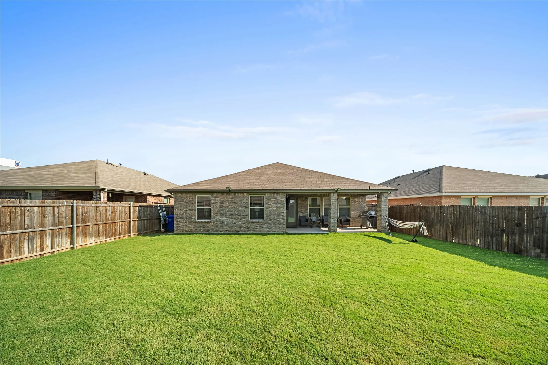 Expansive backyard featuring a manicured lawn, full privacy fencing, and a covered concrete patio