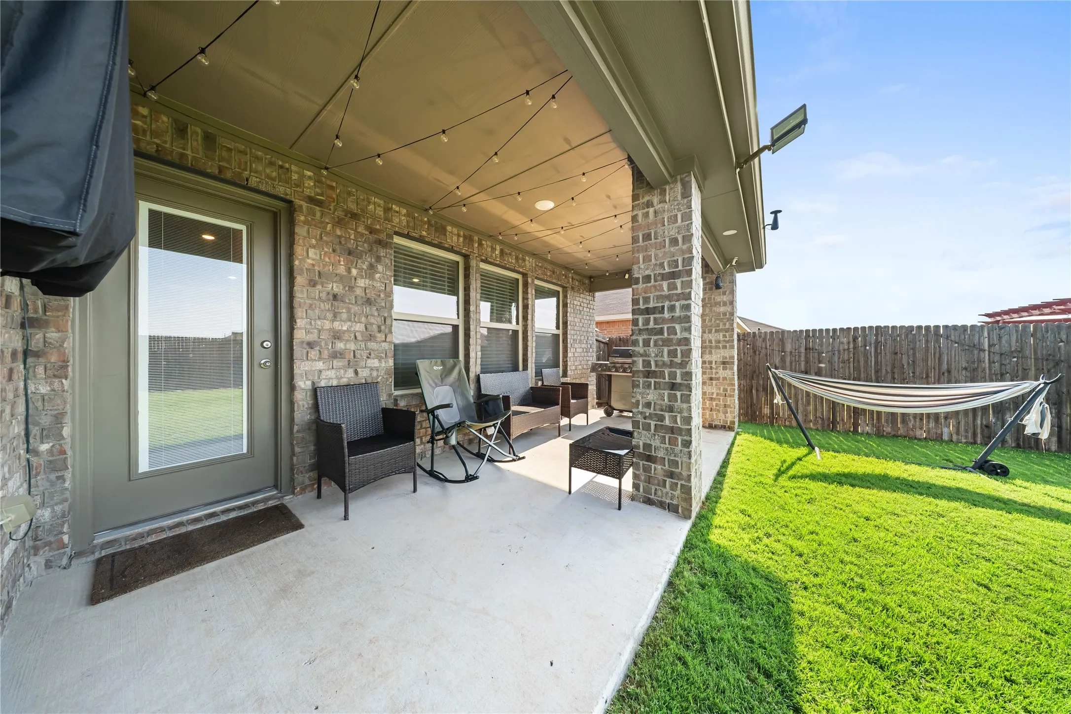 Covered patio featuring string lighting, brick columns, and a concrete surface