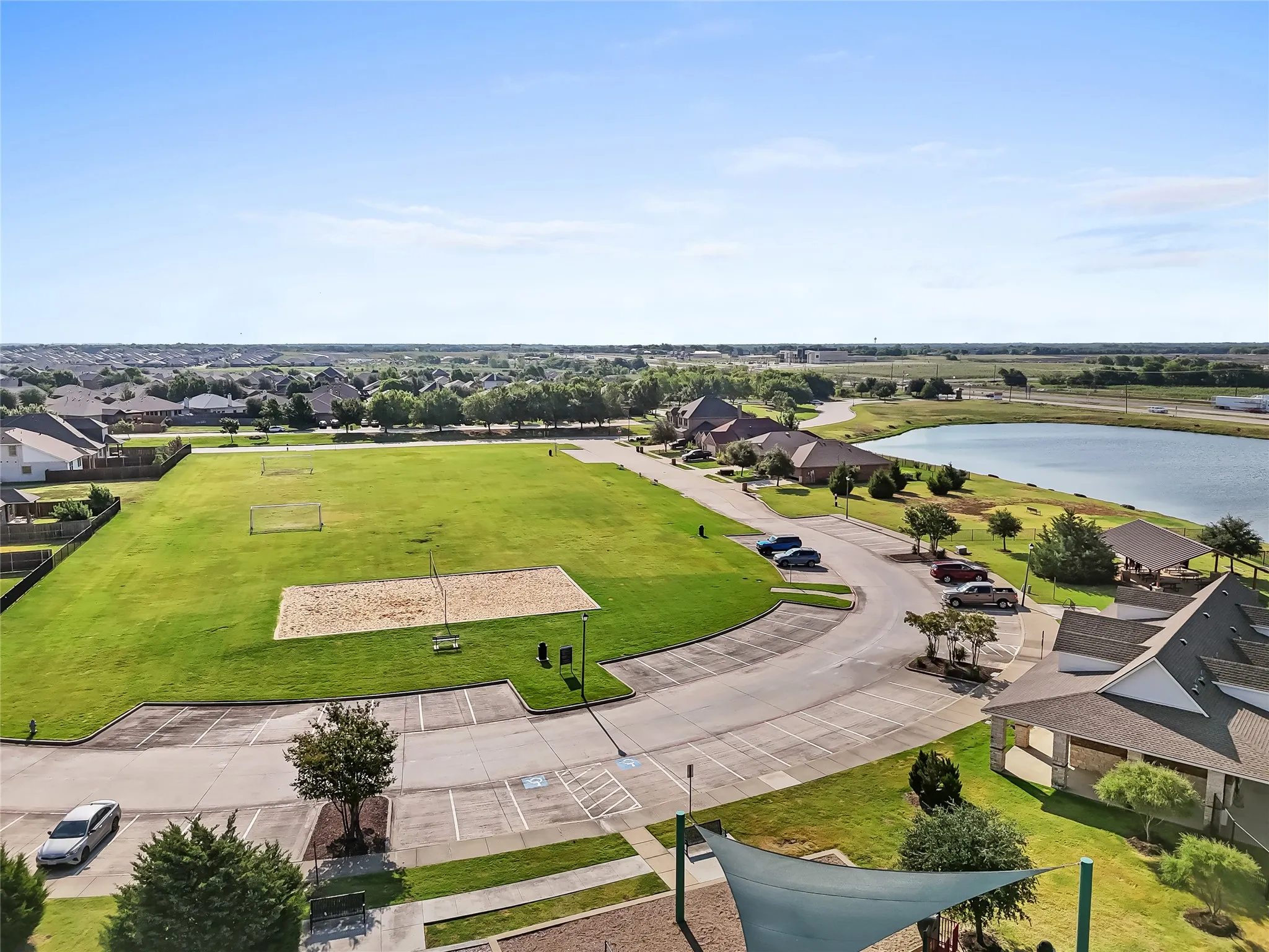 Expansive green space featuring a sand volleyball court, soccer goals, and a paved parking area