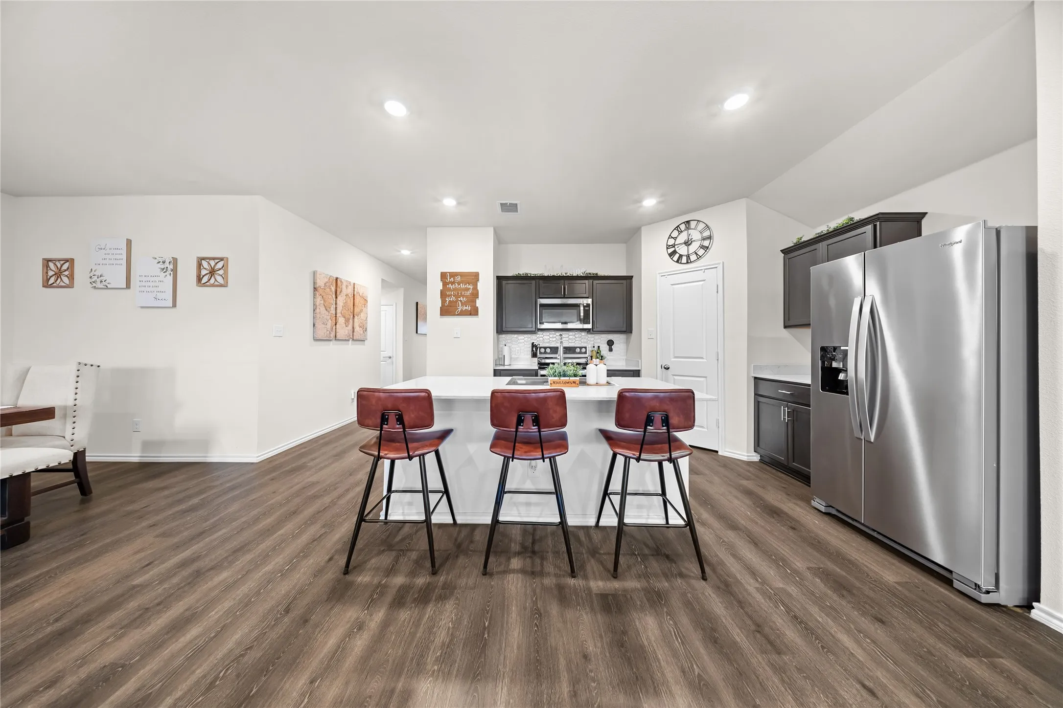 Open-concept kitchen featuring an island with seating, stainless steel appliances, dark wood cabinetry, light countertops, and wood-finish flooring