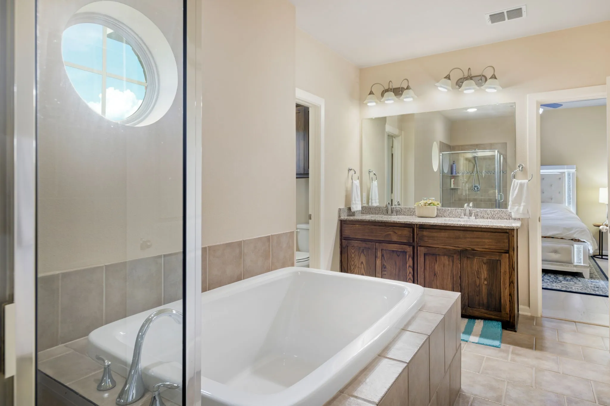 Bathroom with a built-in tub featuring deck-mounted fixtures, a dual-sink vanity with a light-toned countertop, and a large wall-mounted mirror