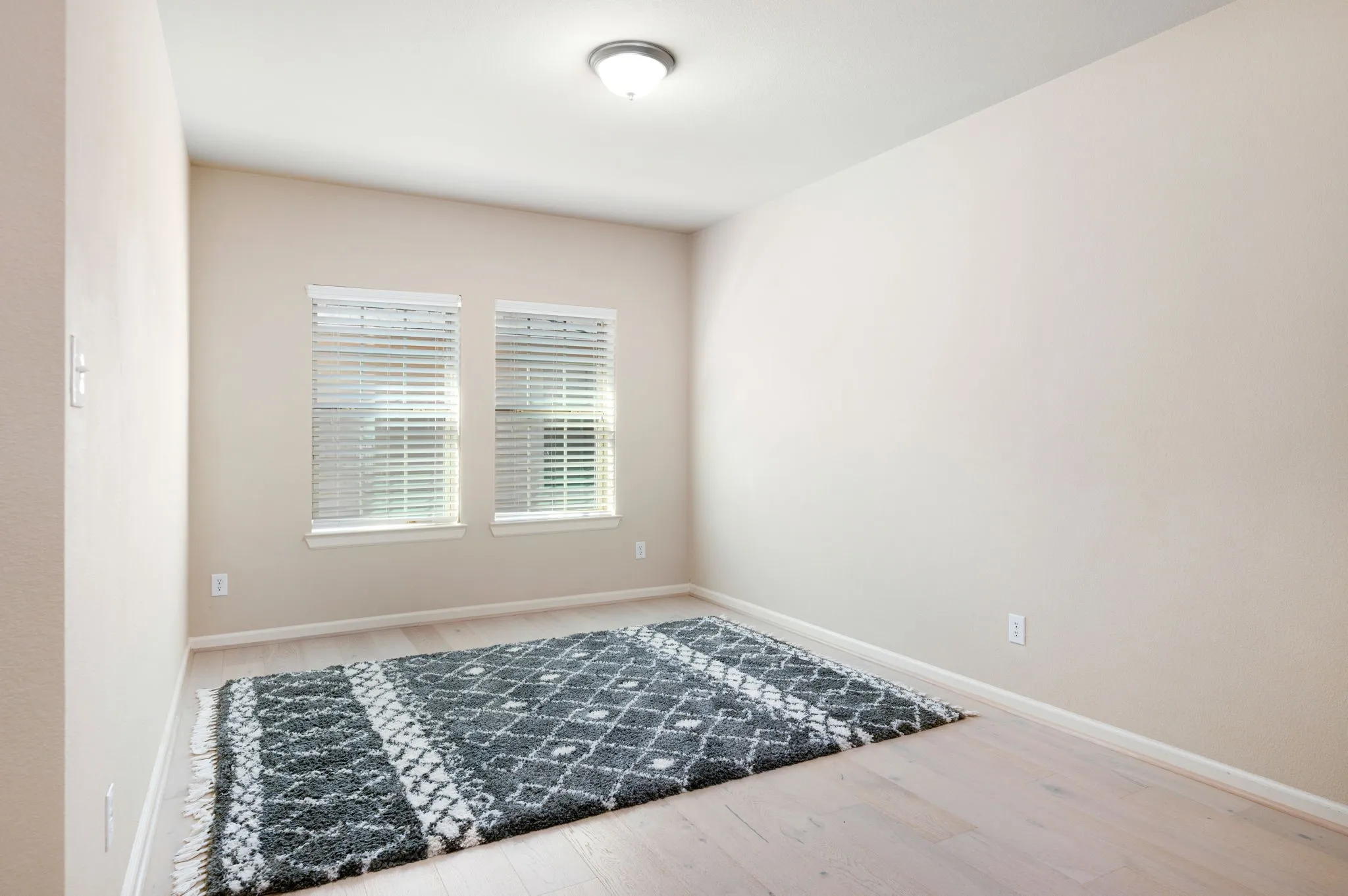 Room featuring light wood-finish flooring, neutral wall paint, and two windows with blinds