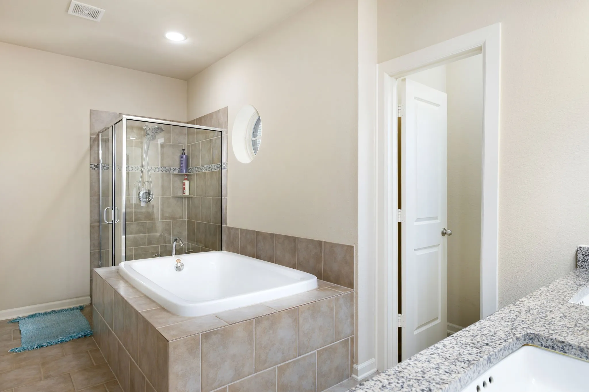 Built-in bathtub with surrounding tile, glass-enclosed shower, dual vanity with undermount sinks, and granite-finish countertop