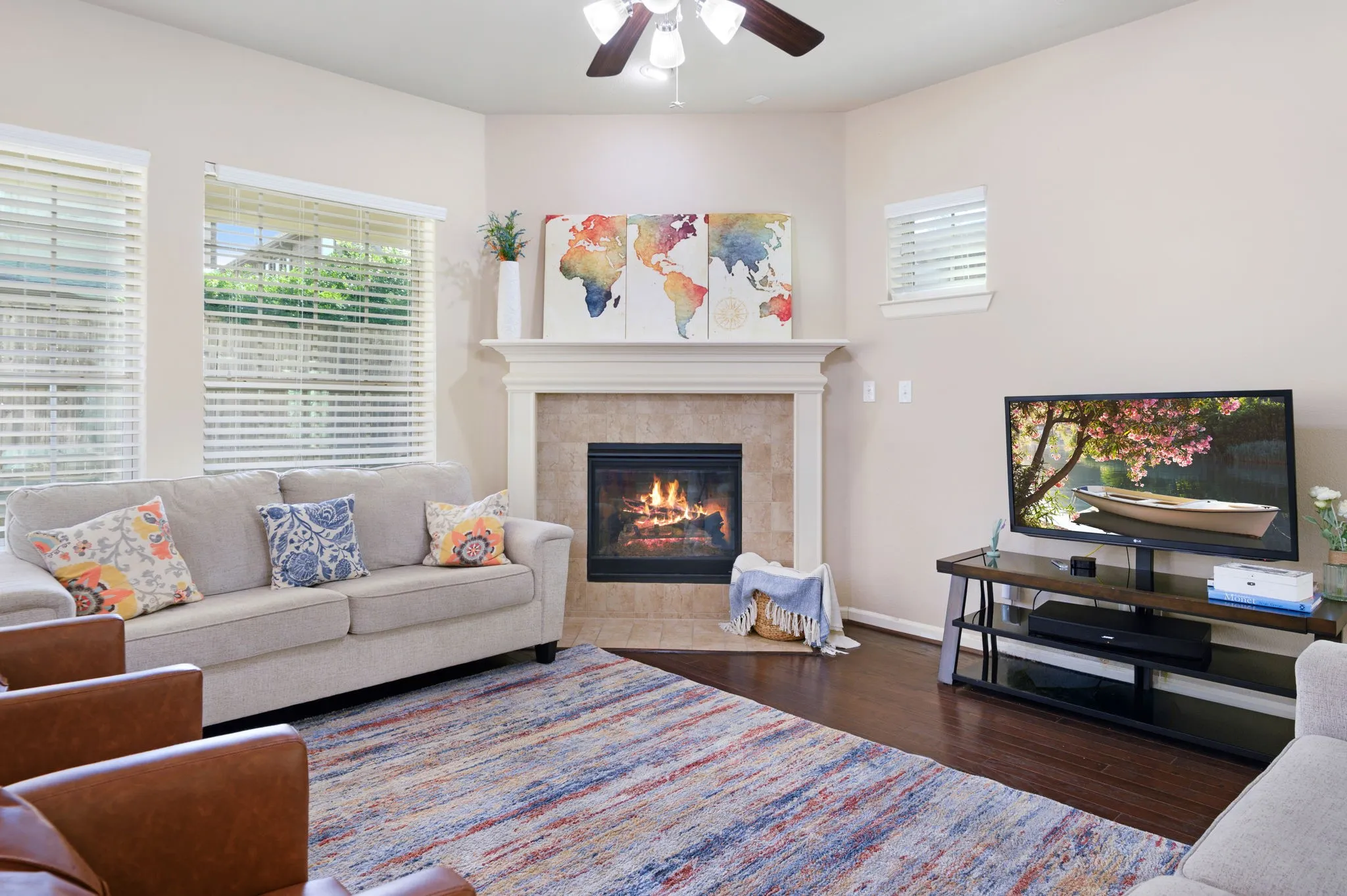 Living area featuring a fireplace with a tile surround and mantel, rich wood-finish flooring, and multiple windows with blinds