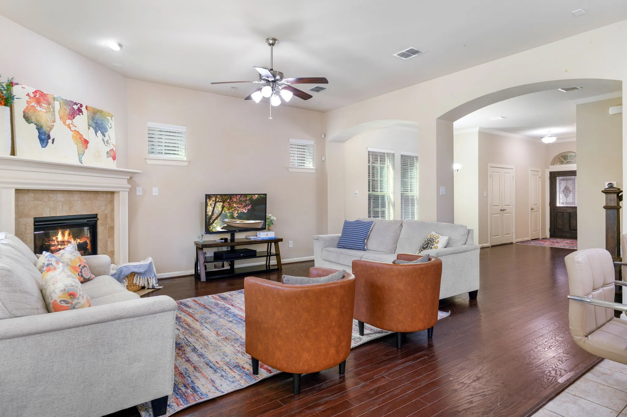 Spacious living area featuring wood-finish flooring, a fireplace with a stone surround and mantel, and a ceiling fan