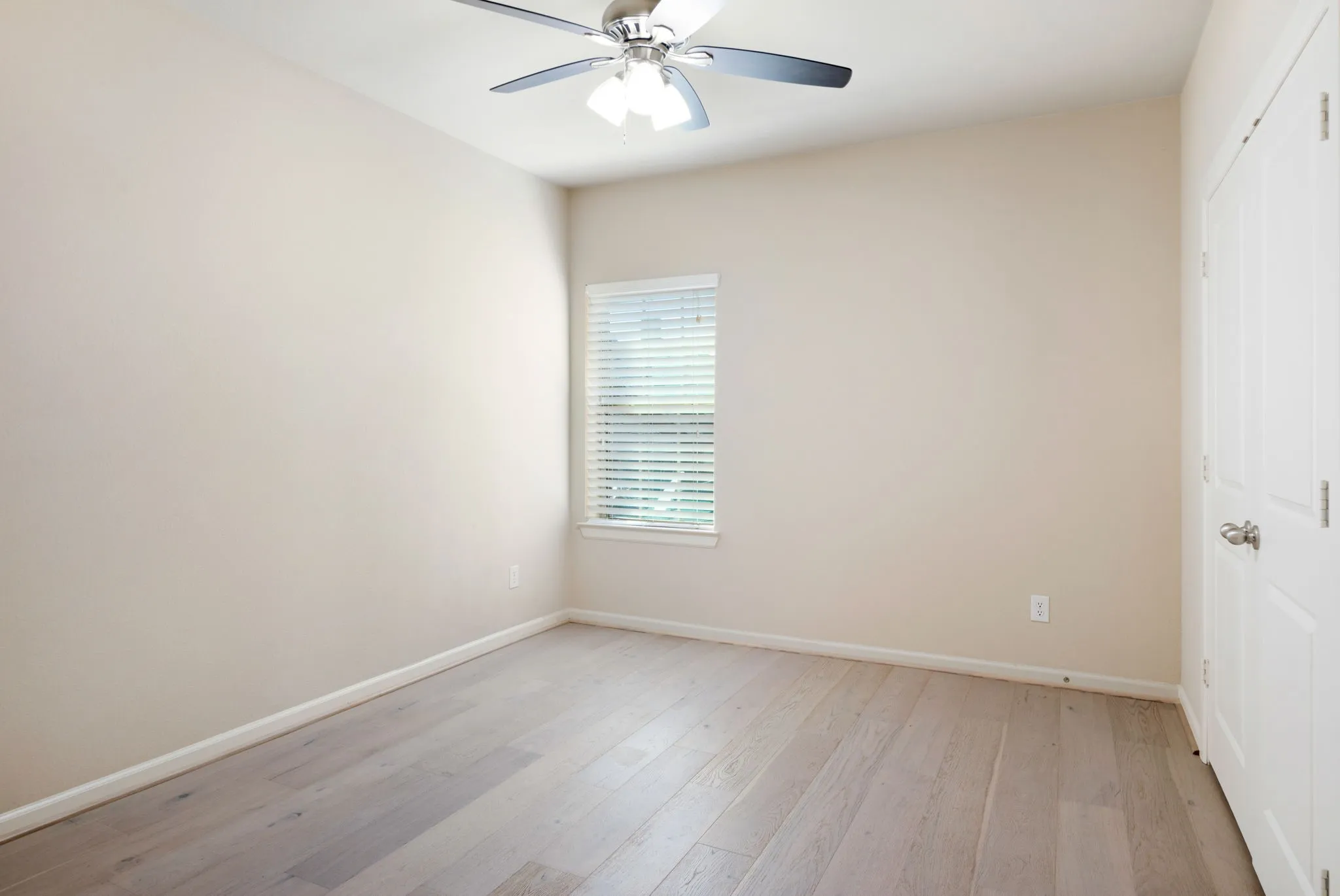 Room featuring light wood-finish flooring, a window with horizontal blinds, and a white paneled door