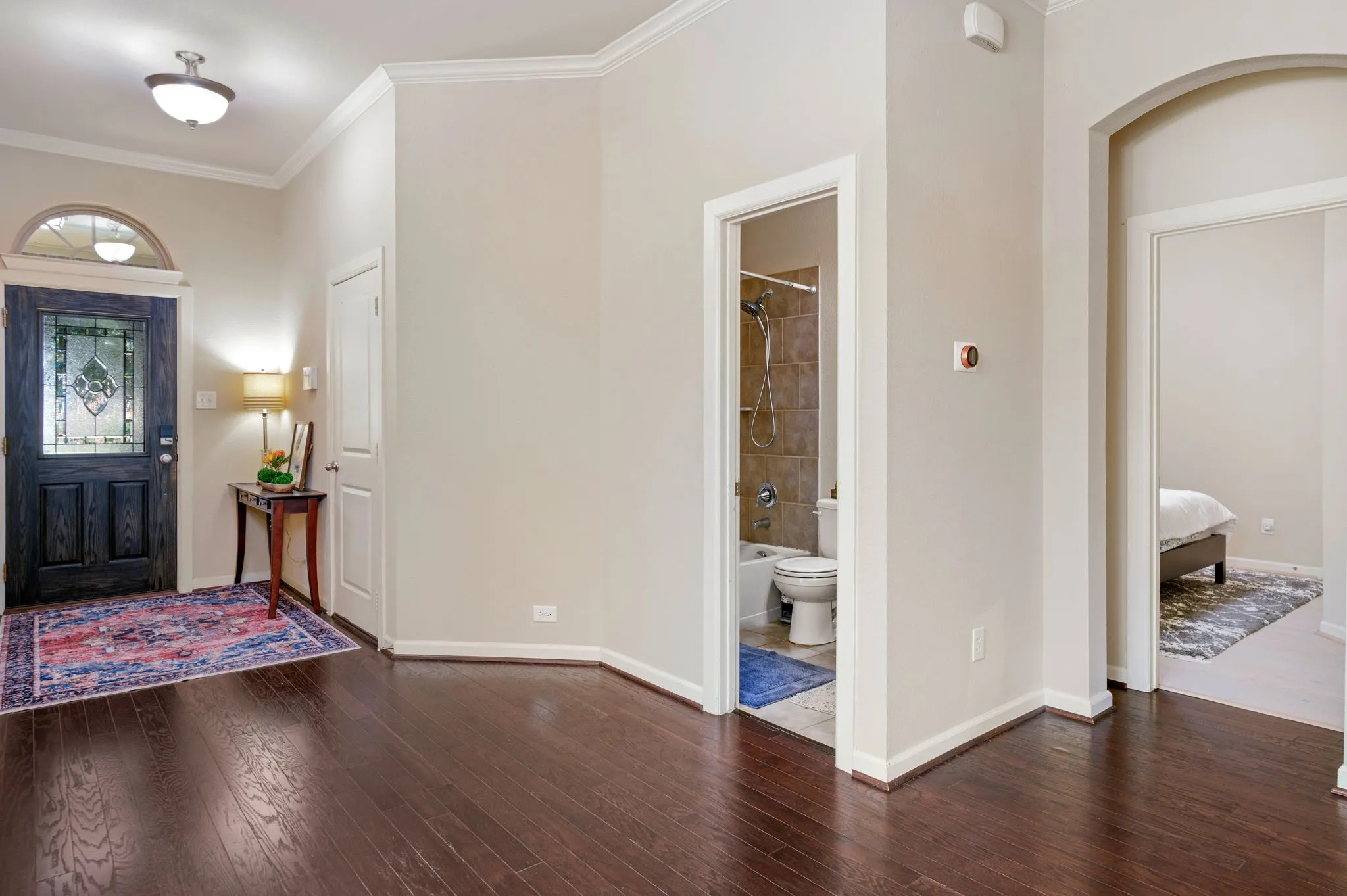 Entryway with rich wood-finish flooring, crown molding, and a front door featuring decorative glass and an arched transom window
