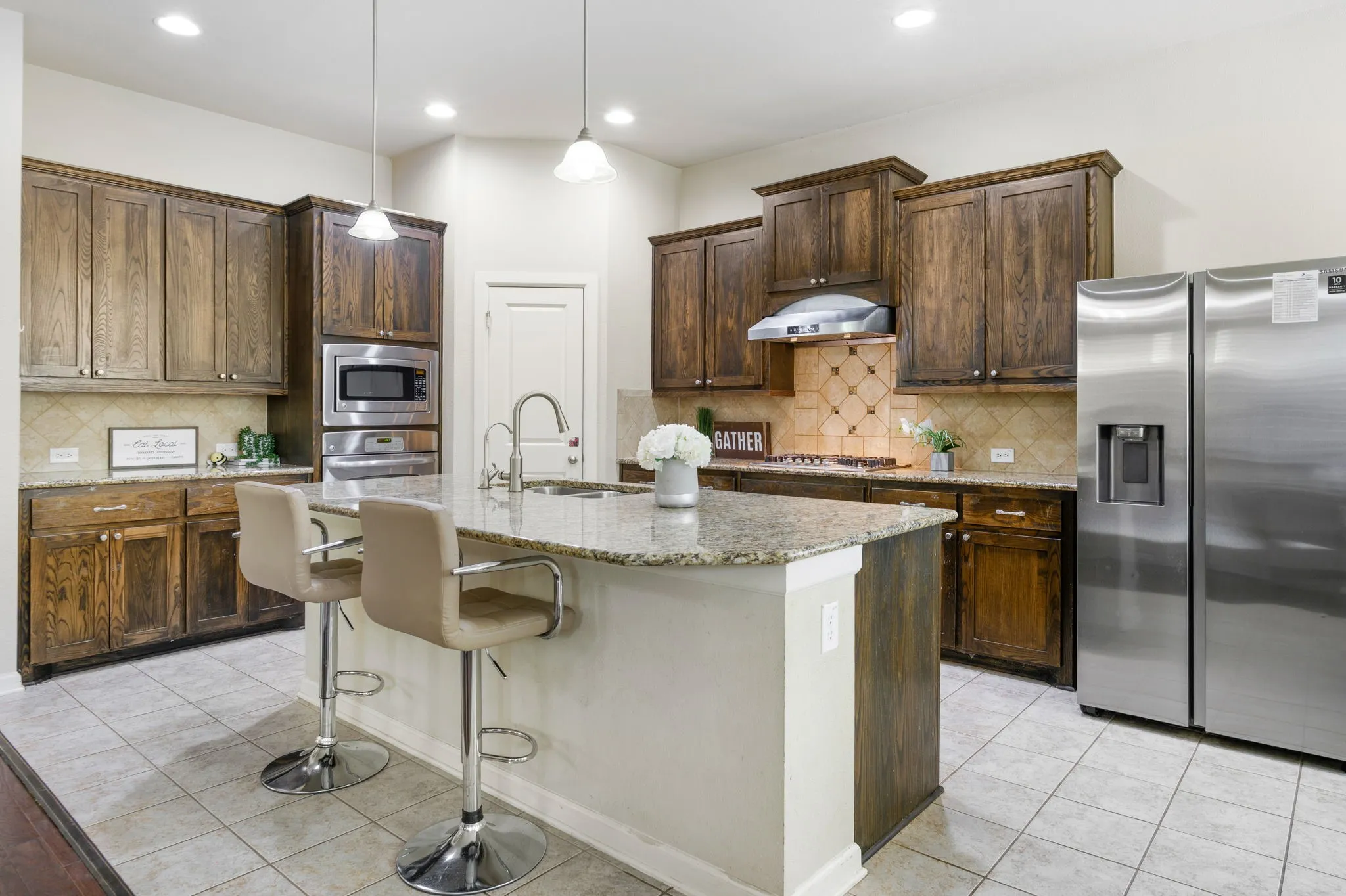 Kitchen featuring a central island with a granite countertop, dark wood-finish cabinetry, stainless steel appliances, a patterned tile backsplash, and recessed lighting