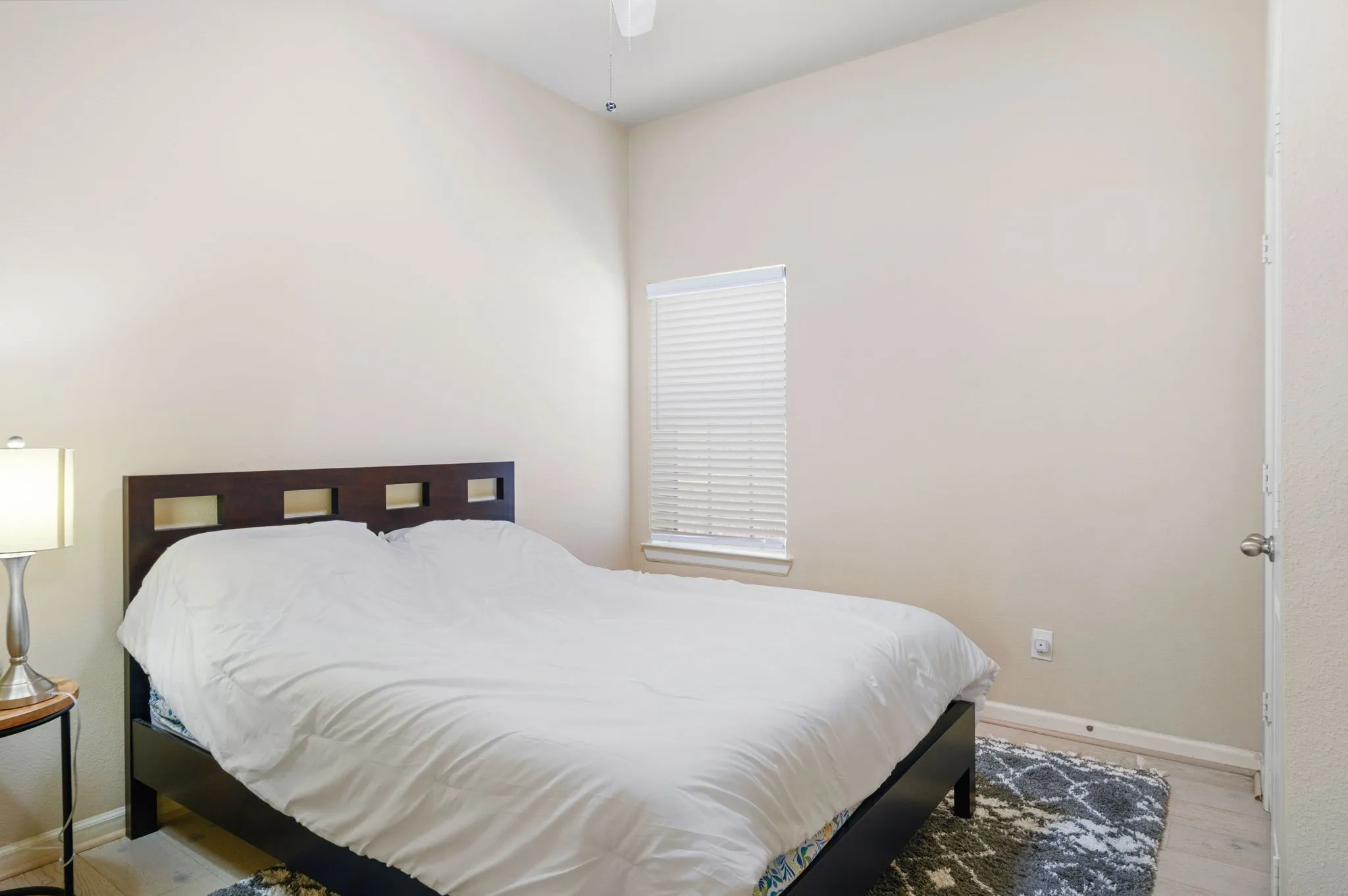 Neutral wall tones with a window featuring blinds, wood-finish flooring, and a ceiling fan