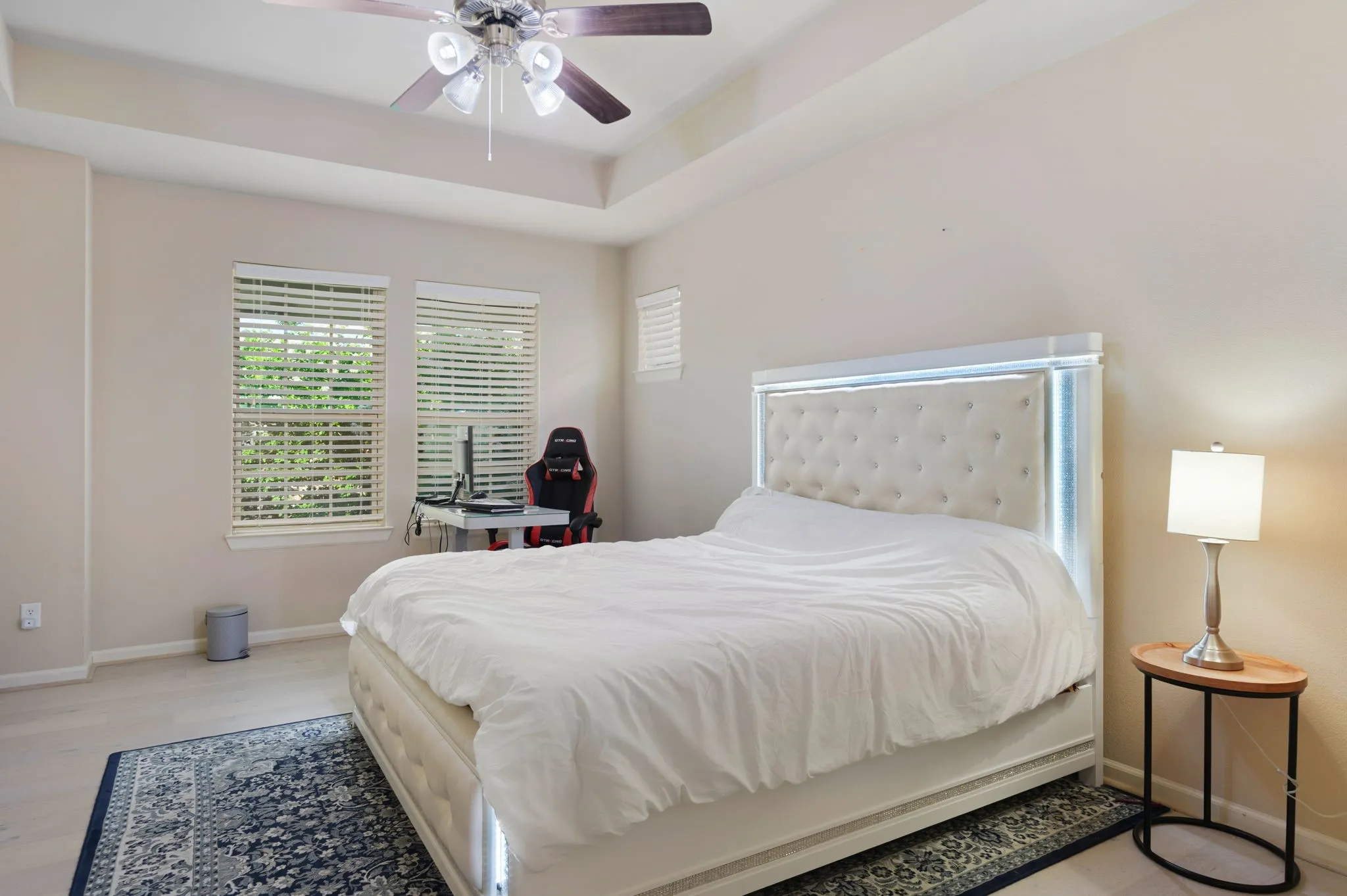 Spacious room featuring a tray ceiling with a ceiling fan, two windows with blinds, and light-toned walls