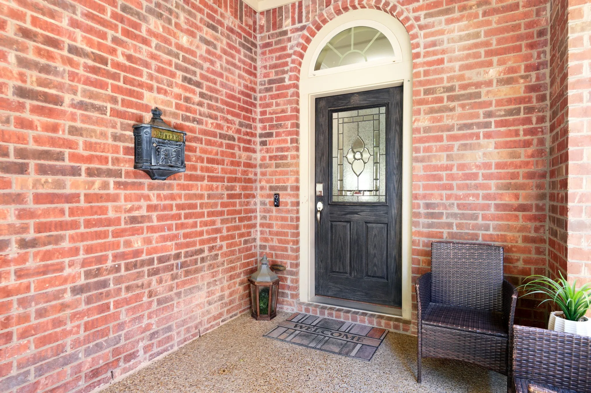 Brick exterior with a dark wood-finish entry door featuring a decorative glass insert and an arched transom window