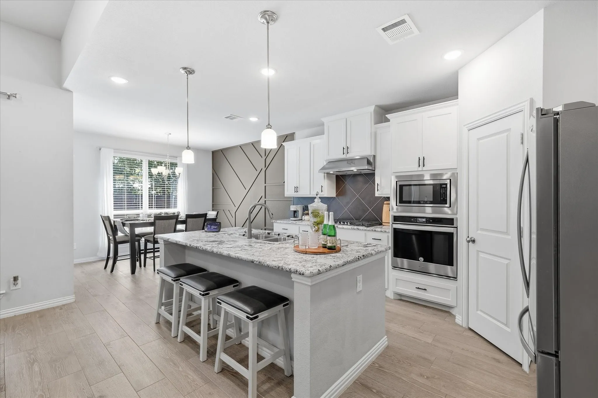 Open-concept kitchen and dining area featuring a kitchen island with seating, pendant lighting, stainless steel appliances, white cabinetry, and wood-finish flooring