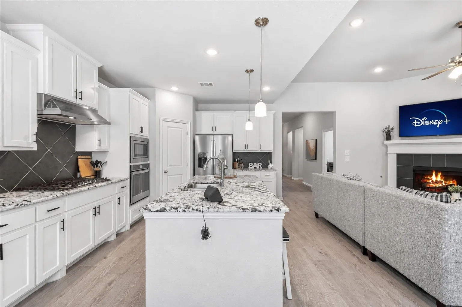 Modern kitchen with white cabinetry and granite countertops, featuring stainless steel appliances, a center island with pendant lighting, and wood-finish flooring