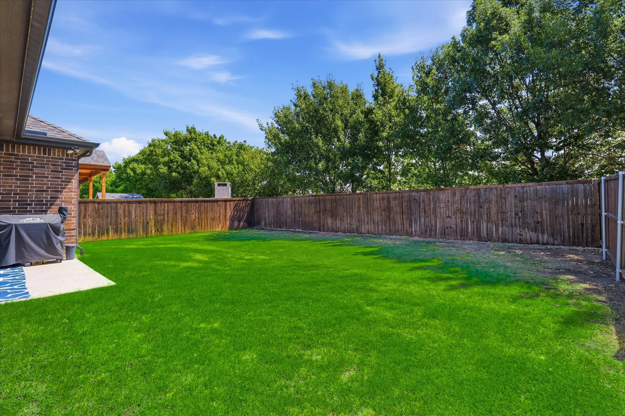 Expansive backyard featuring a lush lawn, a privacy fence, and a concrete patio