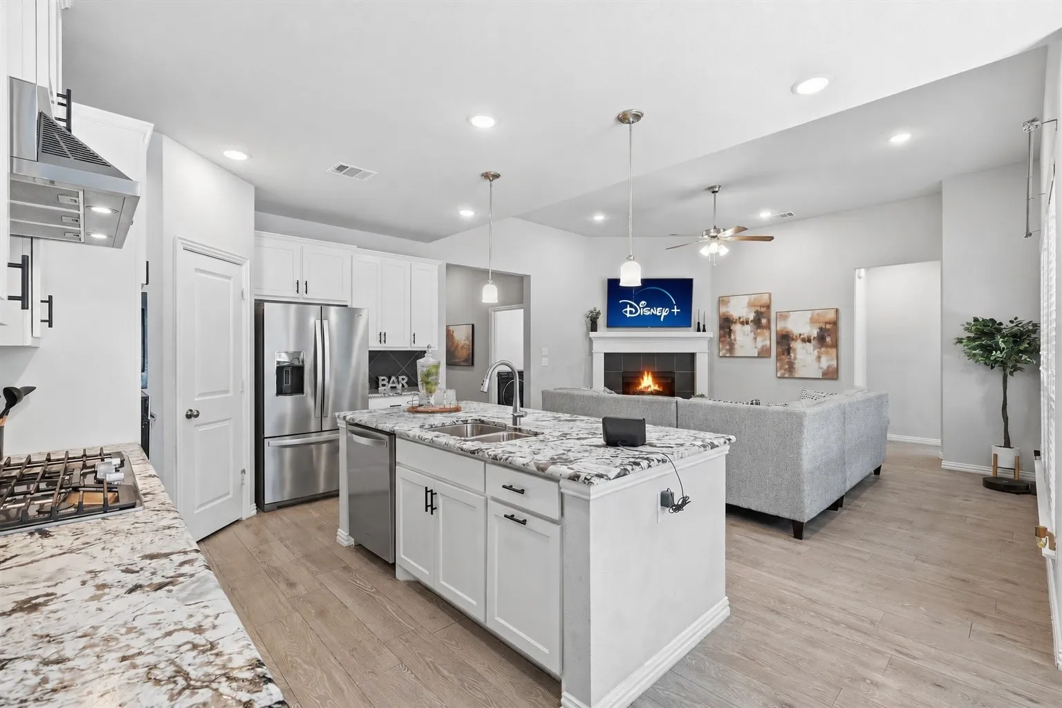 Open-concept kitchen featuring an island with a double basin sink, stainless steel appliances, white cabinetry, and granite countertops