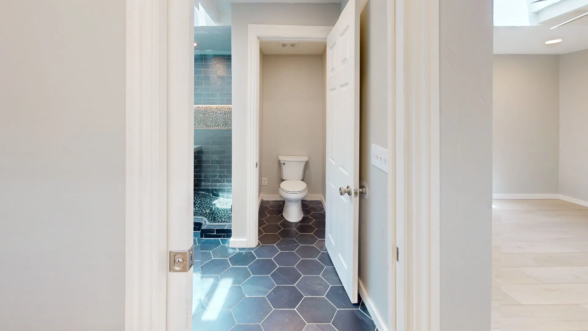 Bathroom featuring dark hexagonal floor tiles, a white toilet, and a glass-enclosed shower with subway tile and pebble flooring
