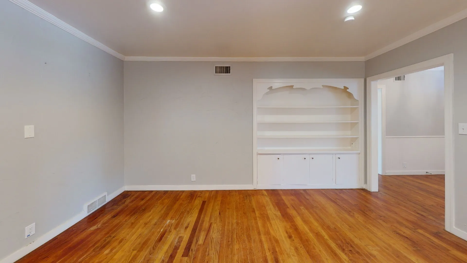 Spacious room featuring wood-finish flooring, light grey walls, and a built-in white shelving unit with lower cabinetry