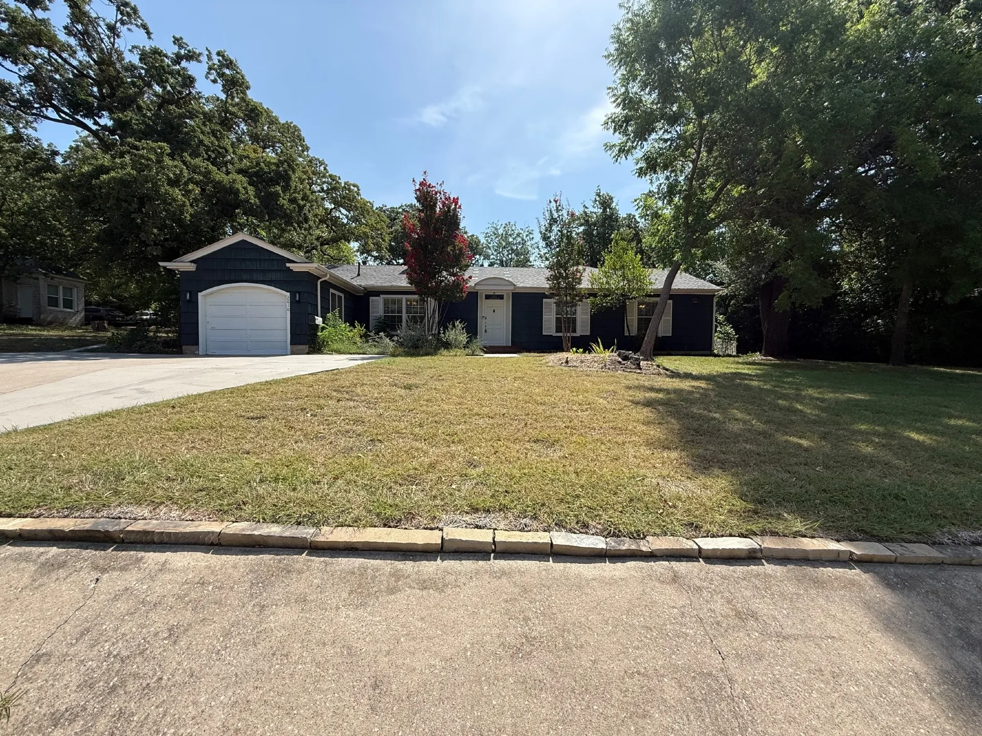 Single-story residence featuring dark blue siding with white trim, an attached garage, a white front door, and a concrete driveway
