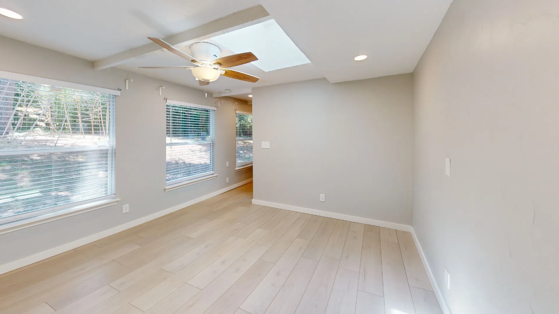 Spacious room featuring wood-finish flooring, multiple windows with blinds, a ceiling fan with light, recessed lighting, and a skylight