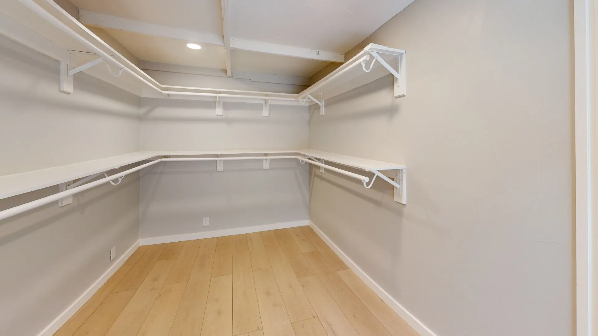 Walk-in closet with light wood-finish flooring, white shelving, and integrated hanging rods