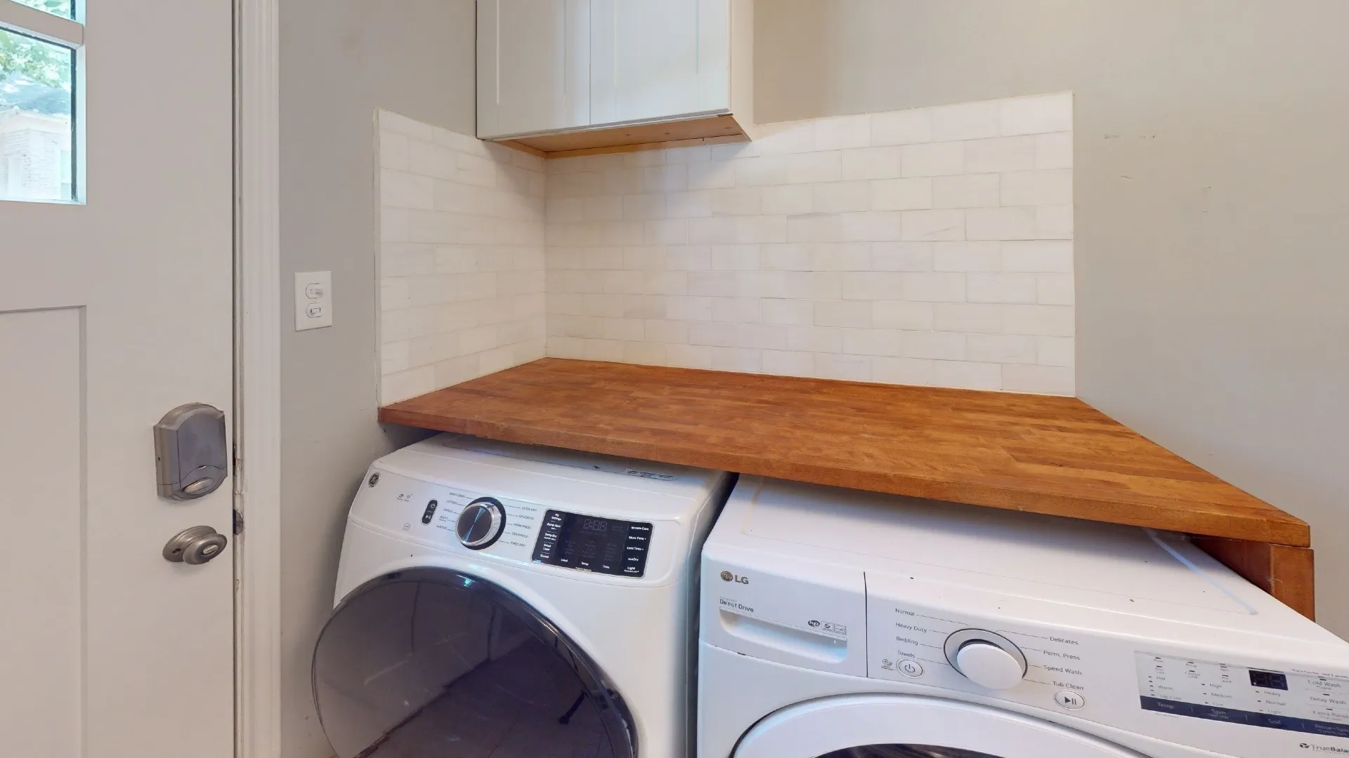 Built-in corner countertop with a wood-finish surface, white subway tile backsplash, and overhead cabinetry