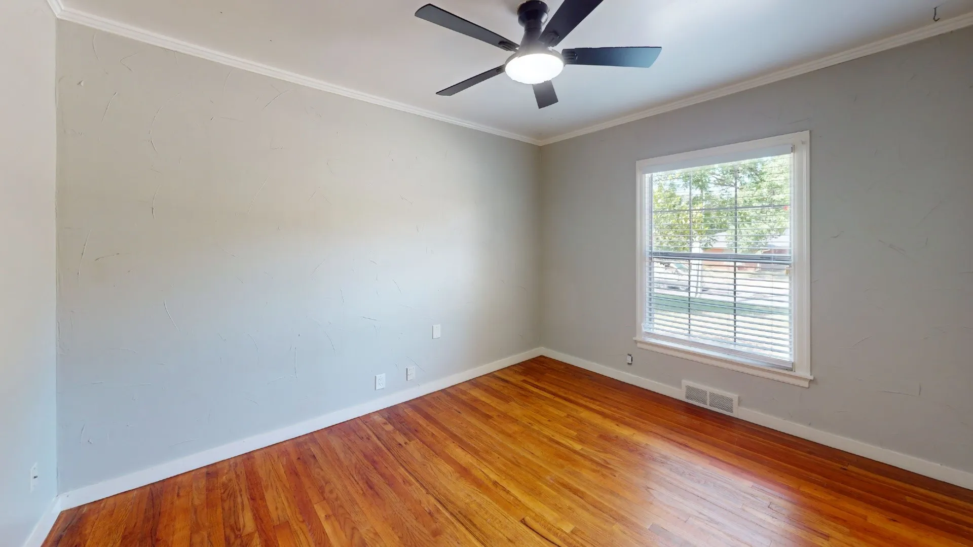 Bright interior room featuring wood-finish flooring, light-toned walls, a ceiling fan with integrated lighting, and a window with blinds