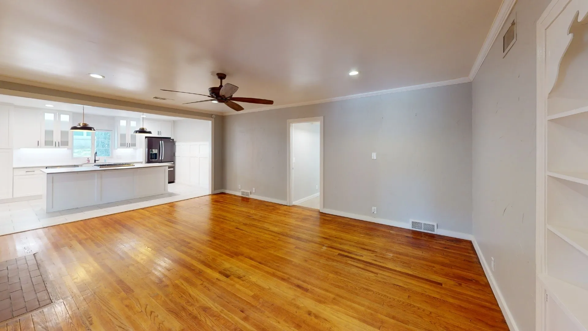 Expansive common area featuring rich wood flooring throughout, built-in shelving, and a ceiling fan