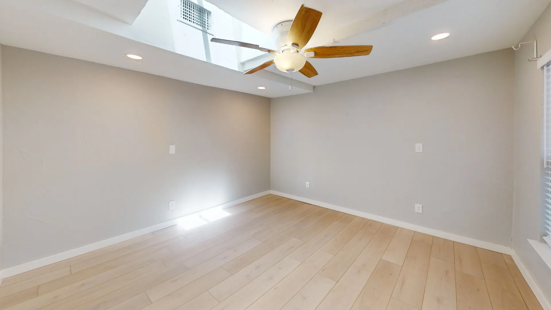 Spacious room featuring wood-finish flooring, a ceiling fan with integrated lighting, recessed lighting, and a large window with blinds