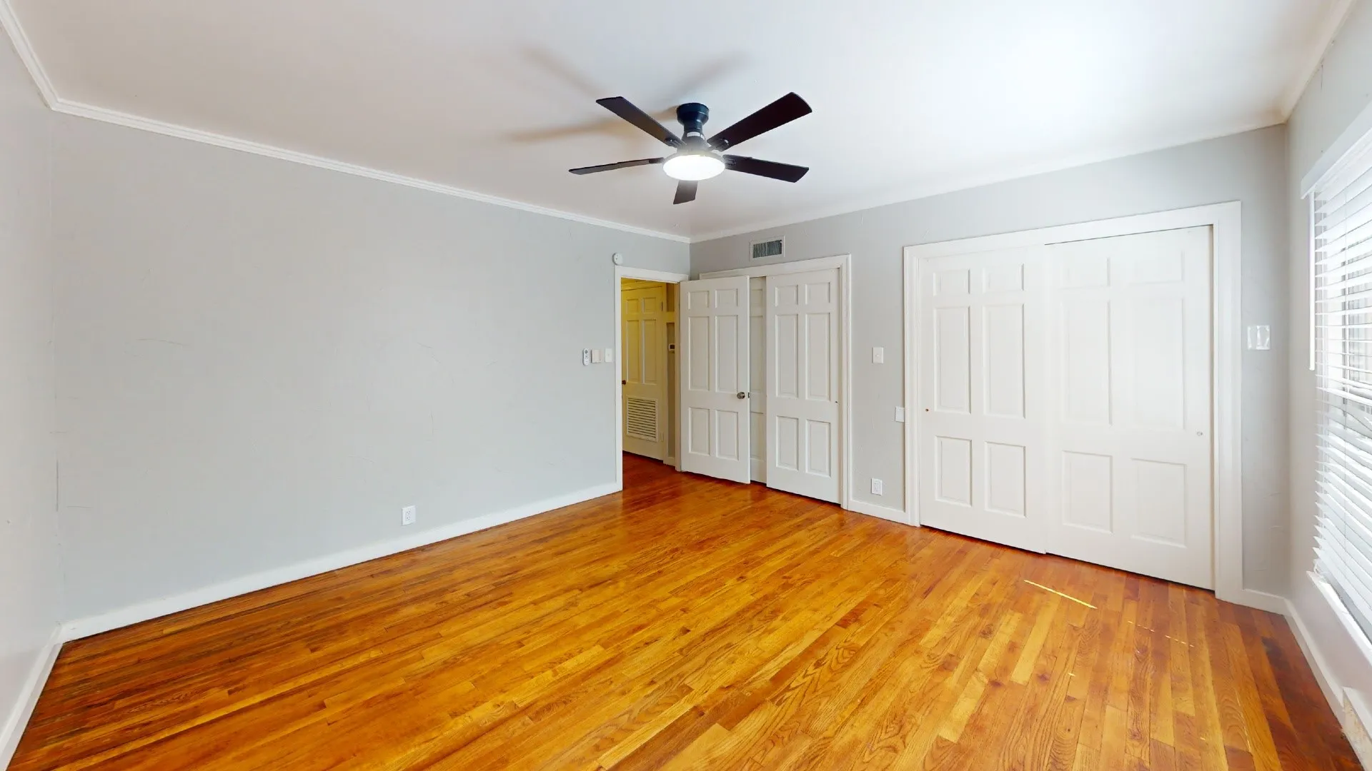 Spacious room featuring wood-finish flooring, a ceiling fan, and sliding panel closet doors