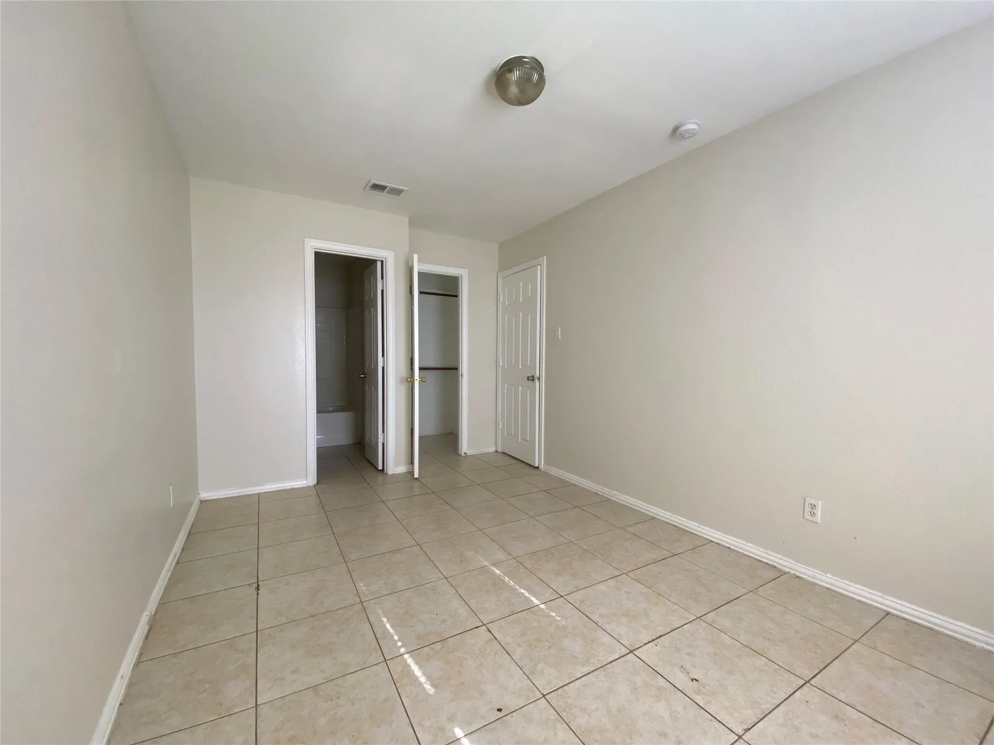 Unfurnished bedroom with ensuite bath and light tile patterned floors