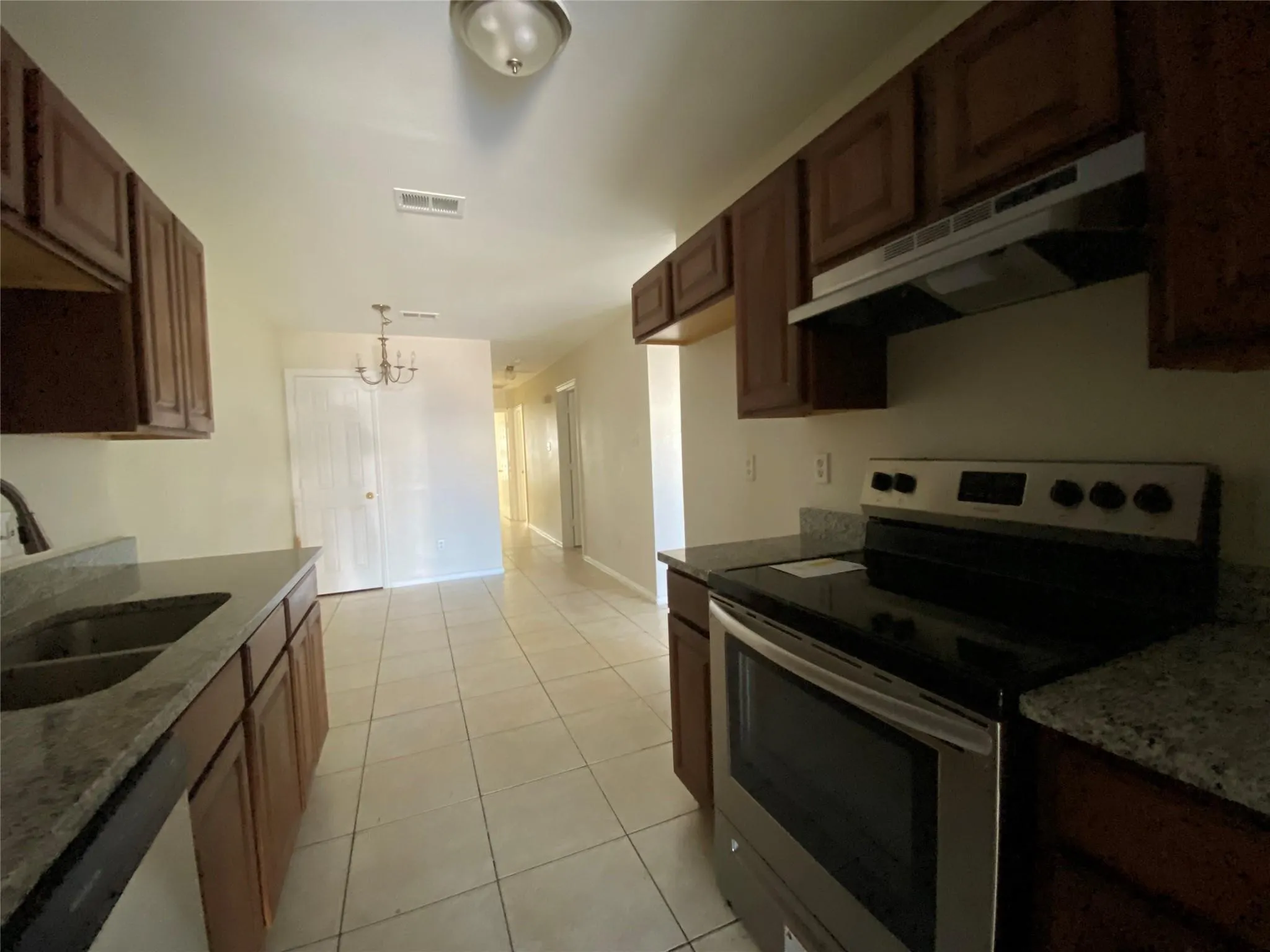 Kitchen featuring dishwasher, sink, stainless steel electric range oven, light tile patterned flooring, and a chandelier