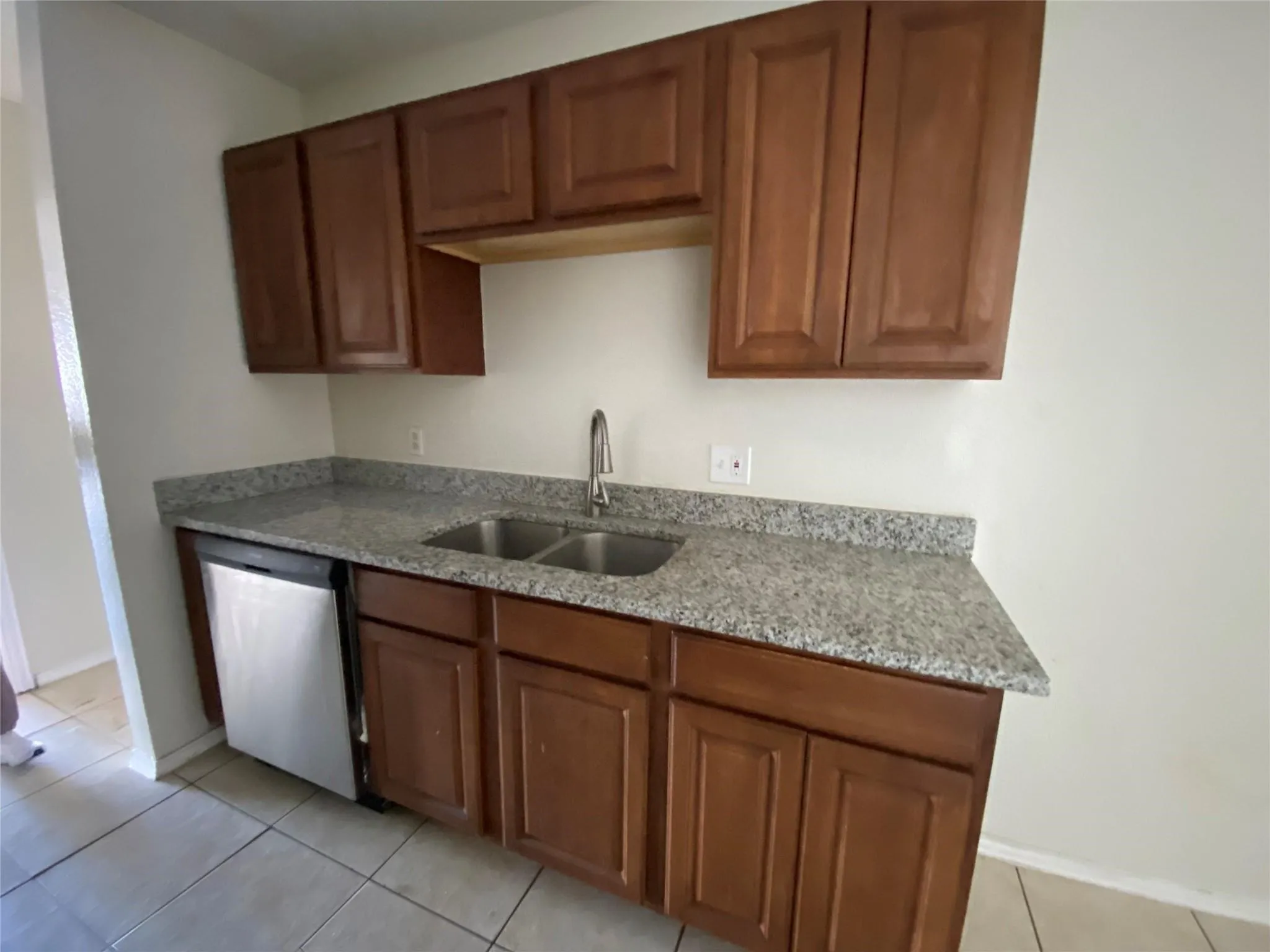 Kitchen with light stone counters, sink, light tile patterned floors, and stainless steel dishwasher