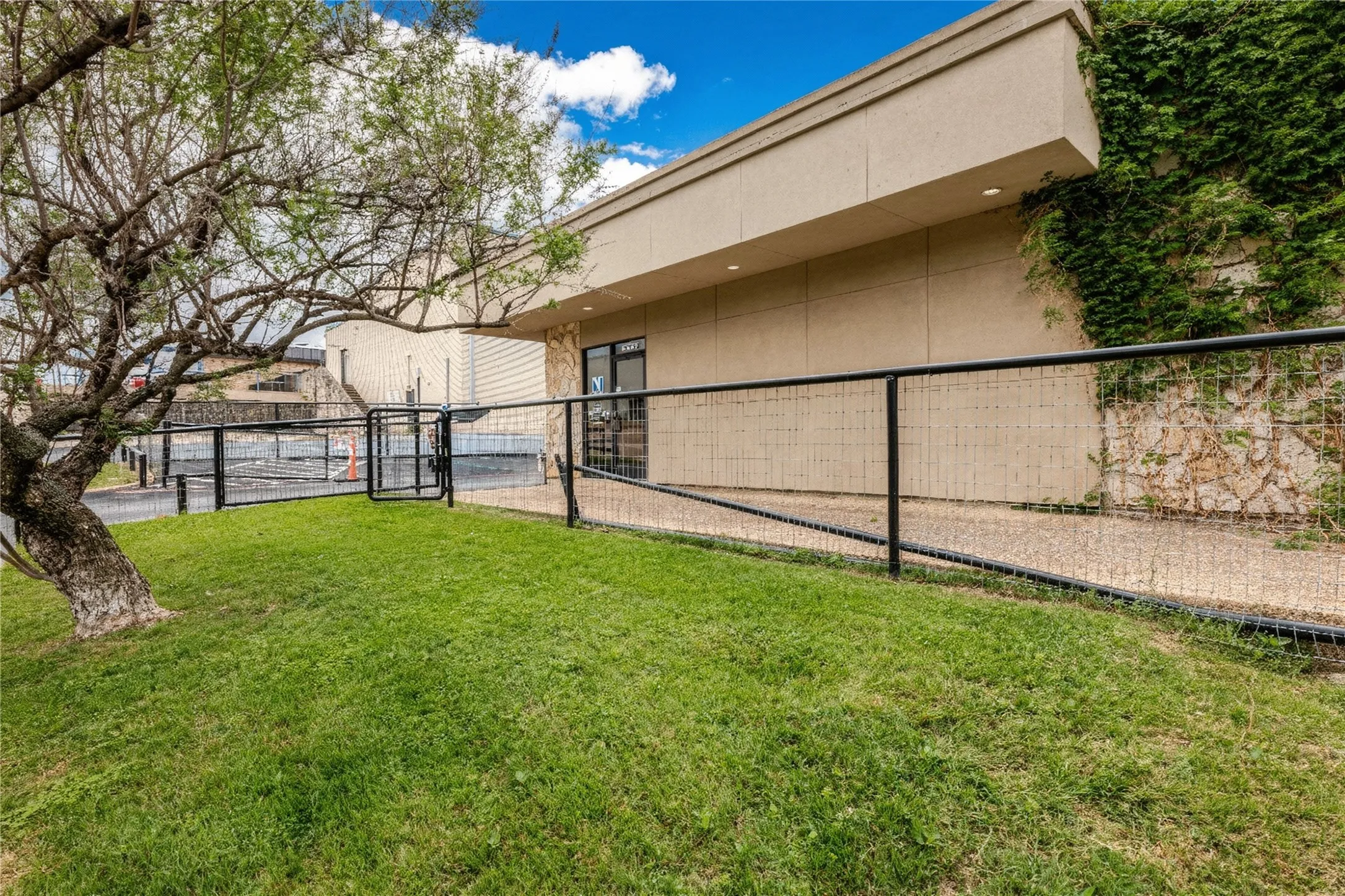 Exterior building featuring a stucco facade, stone accent wall with climbing ivy, and a black metal fence with gate