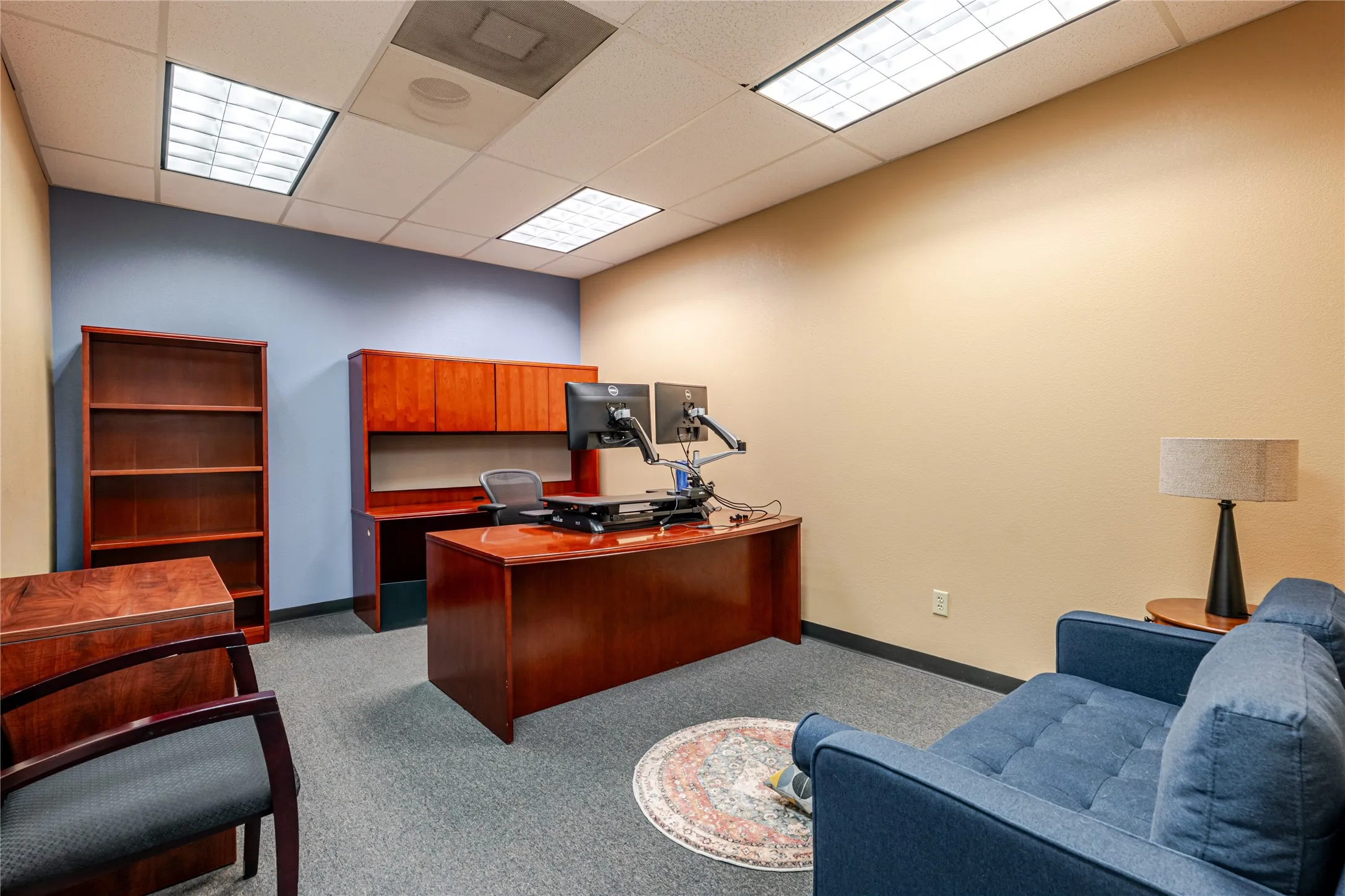Office space featuring commercial-grade carpet flooring, recessed fluorescent lighting, and a suspended acoustic tile ceiling