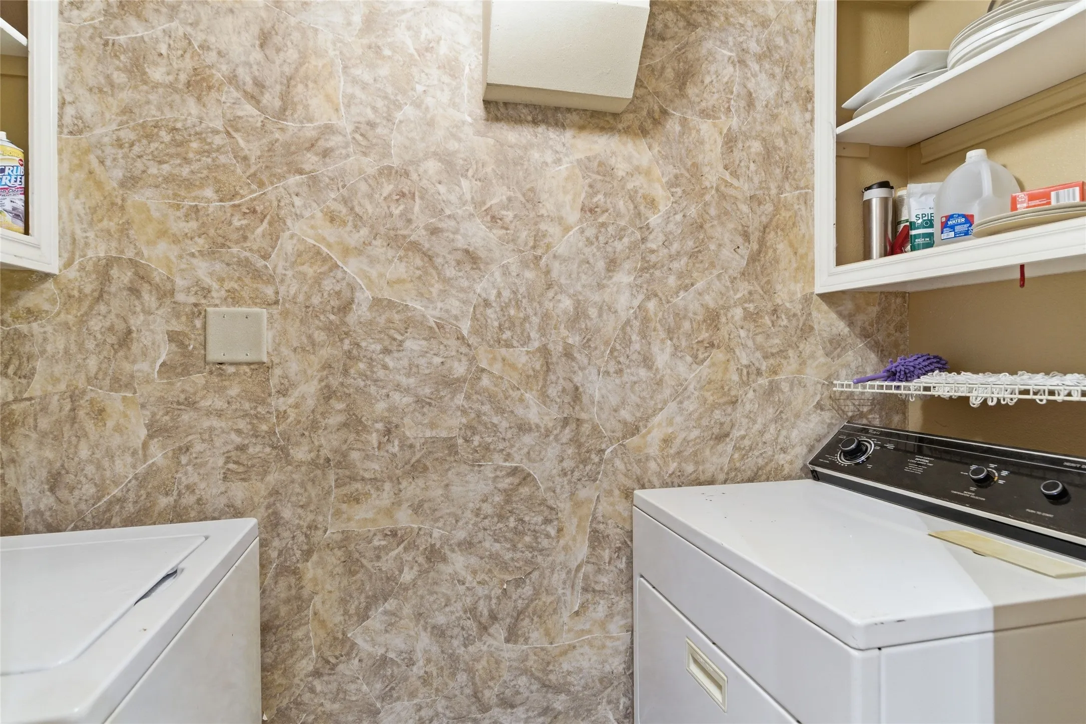 Laundry area featuring neutral-toned wall covering, white upper cabinetry, and a built-in wire shelf