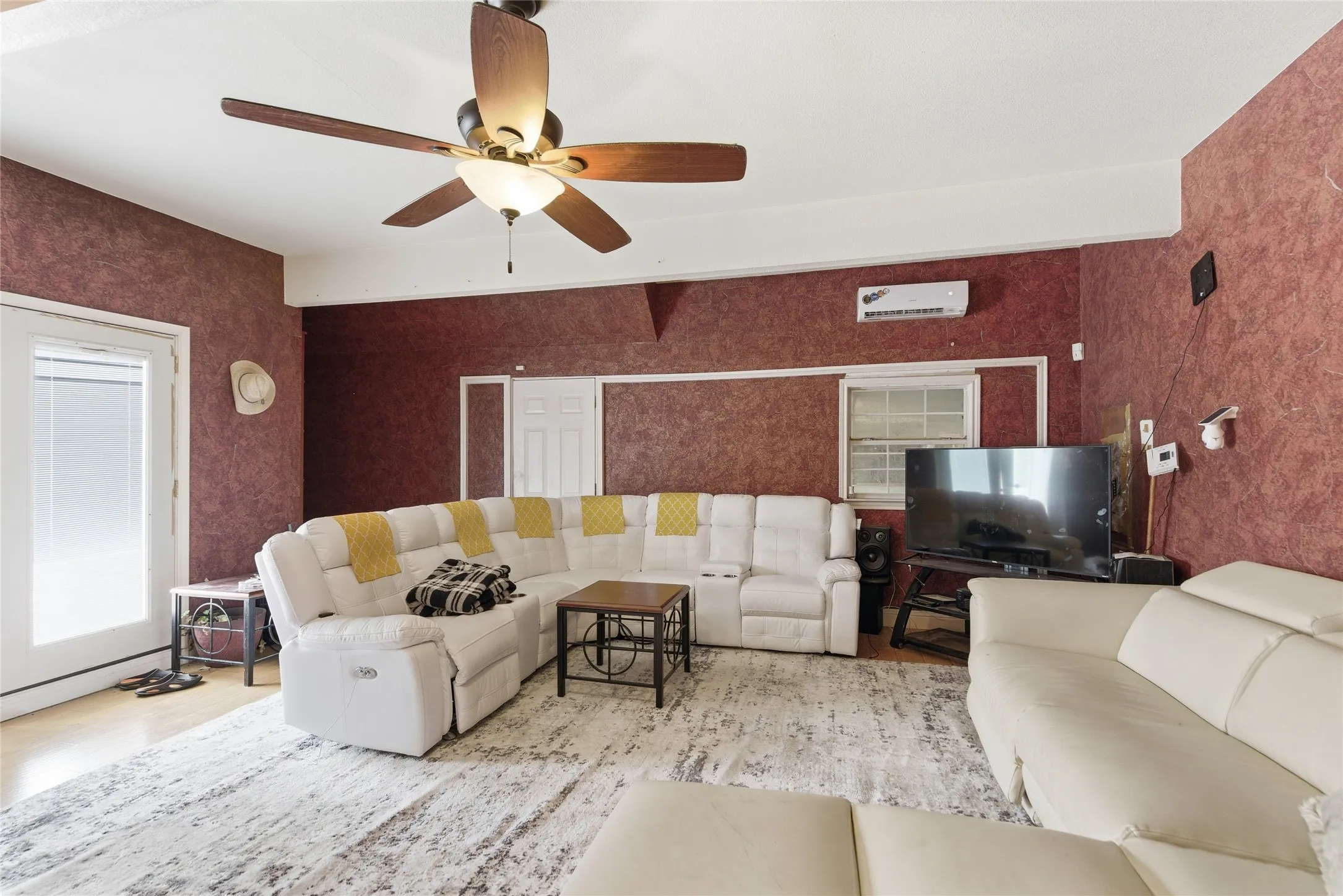 Living area featuring textured red walls, a ceiling fan with integrated lighting, and light wood-finish flooring