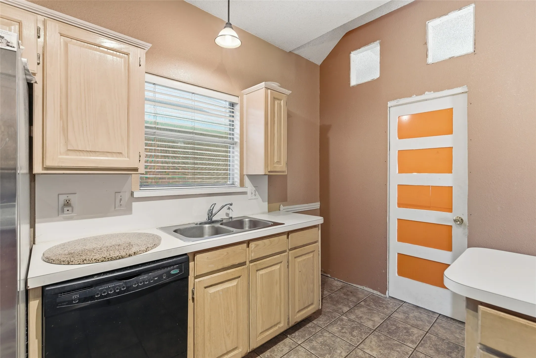 Kitchen featuring a double basin stainless steel sink, black dishwasher, and blonde wood-finish cabinetry