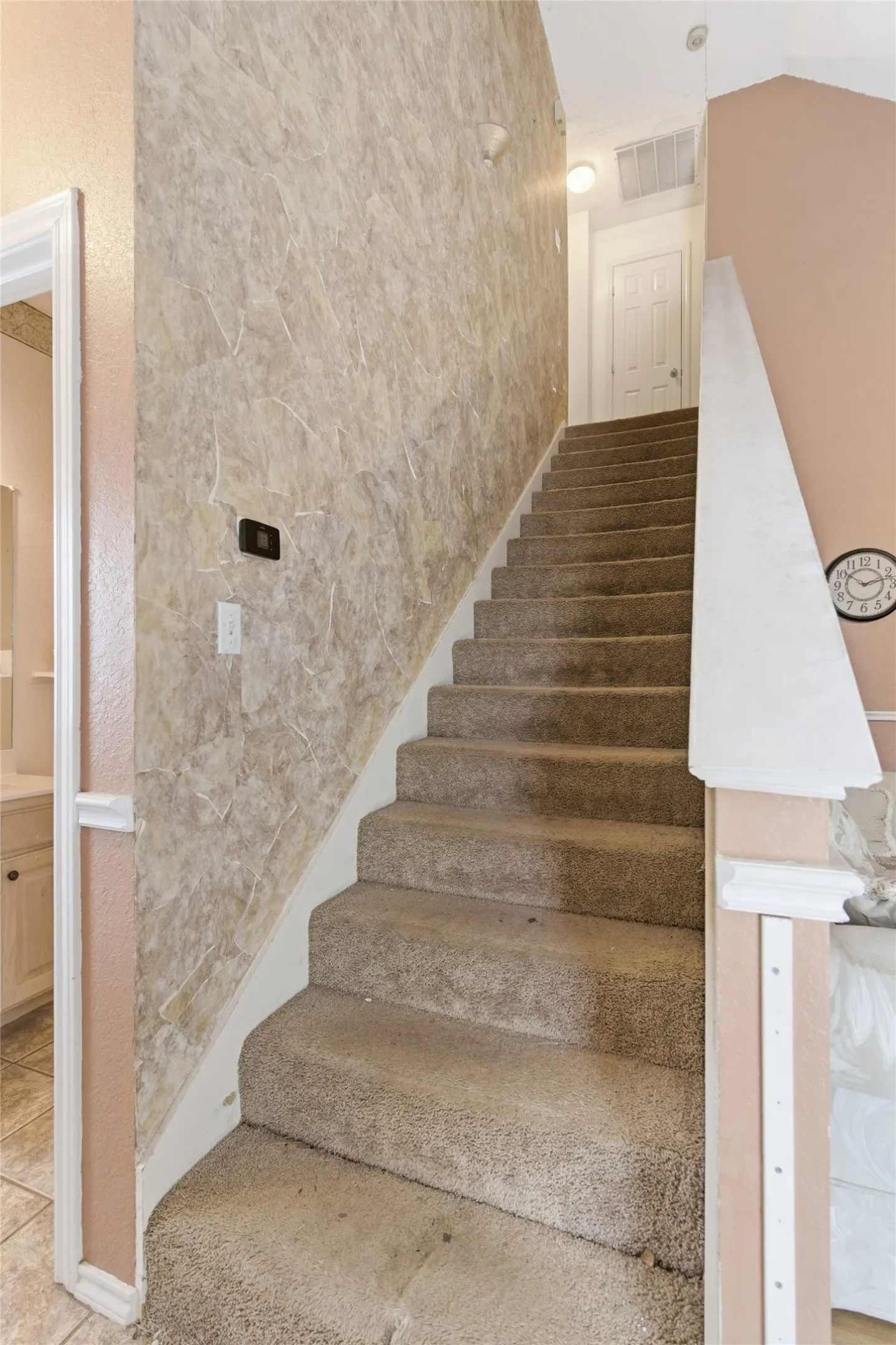 Carpeted staircase with textured wall covering and neutral wall paint