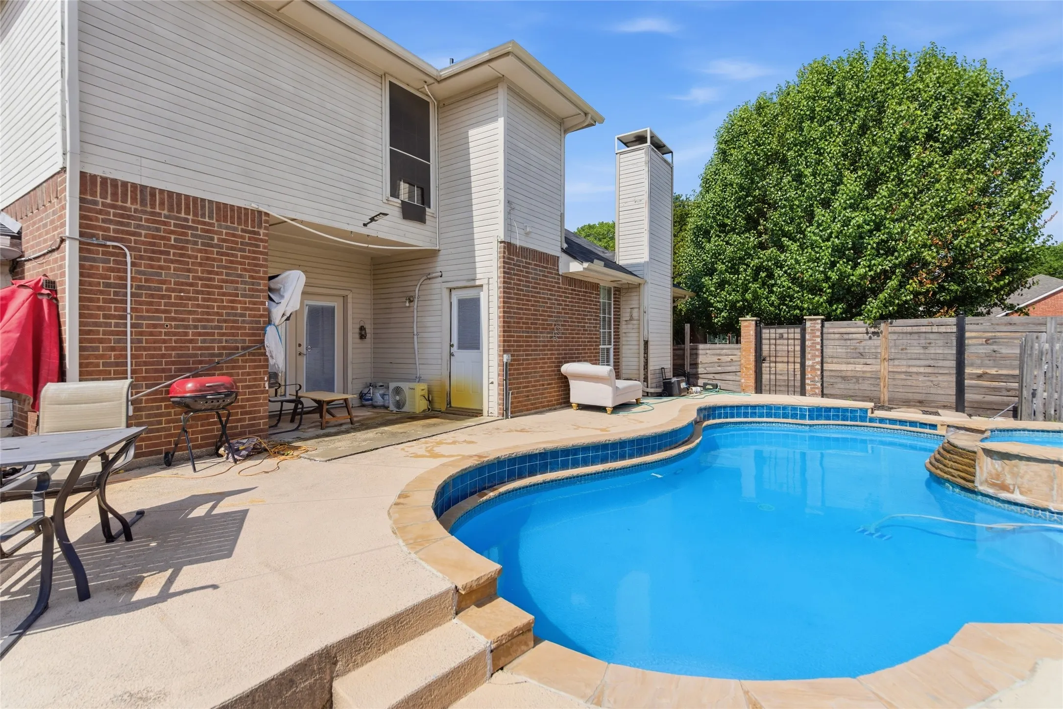 Backyard oasis featuring a curvilinear swimming pool with integrated spa, concrete patio, and a combination brick and siding exterior