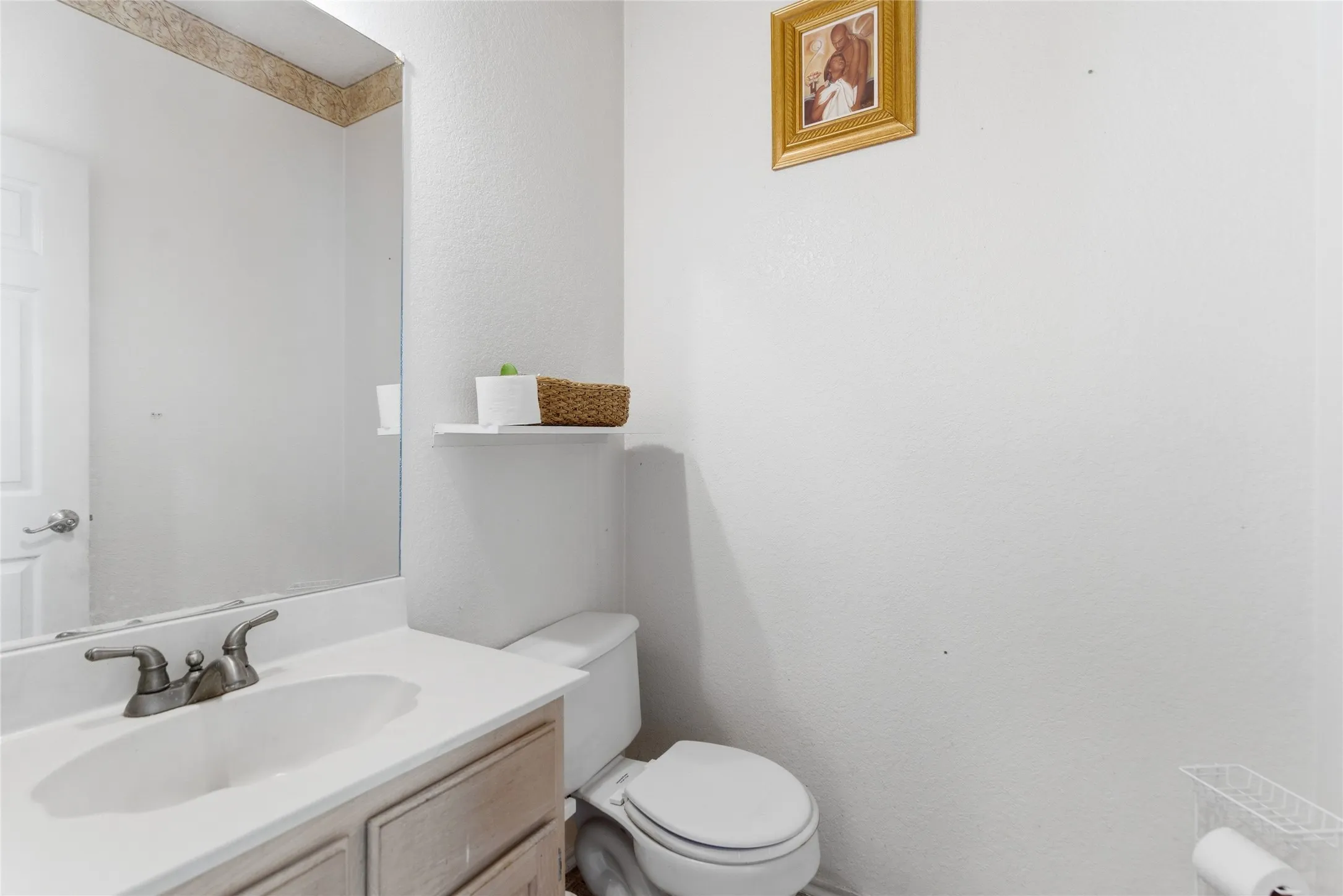 Bathroom featuring a white vanity with an integrated sink, a wall-mounted mirror, and a white toilet