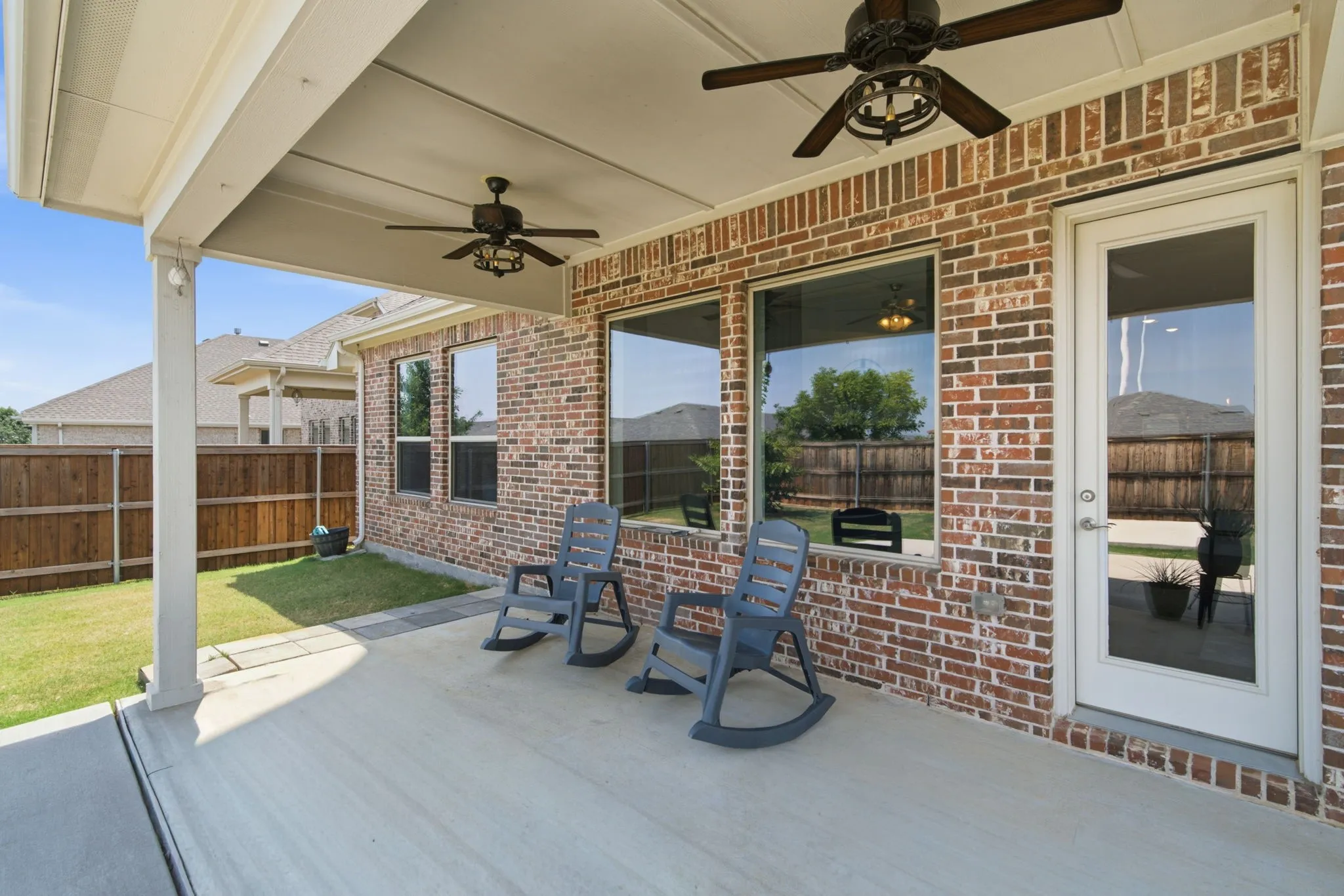 Covered concrete patio with two ceiling fans, brick exterior, multiple windows, and a glass-paneled door