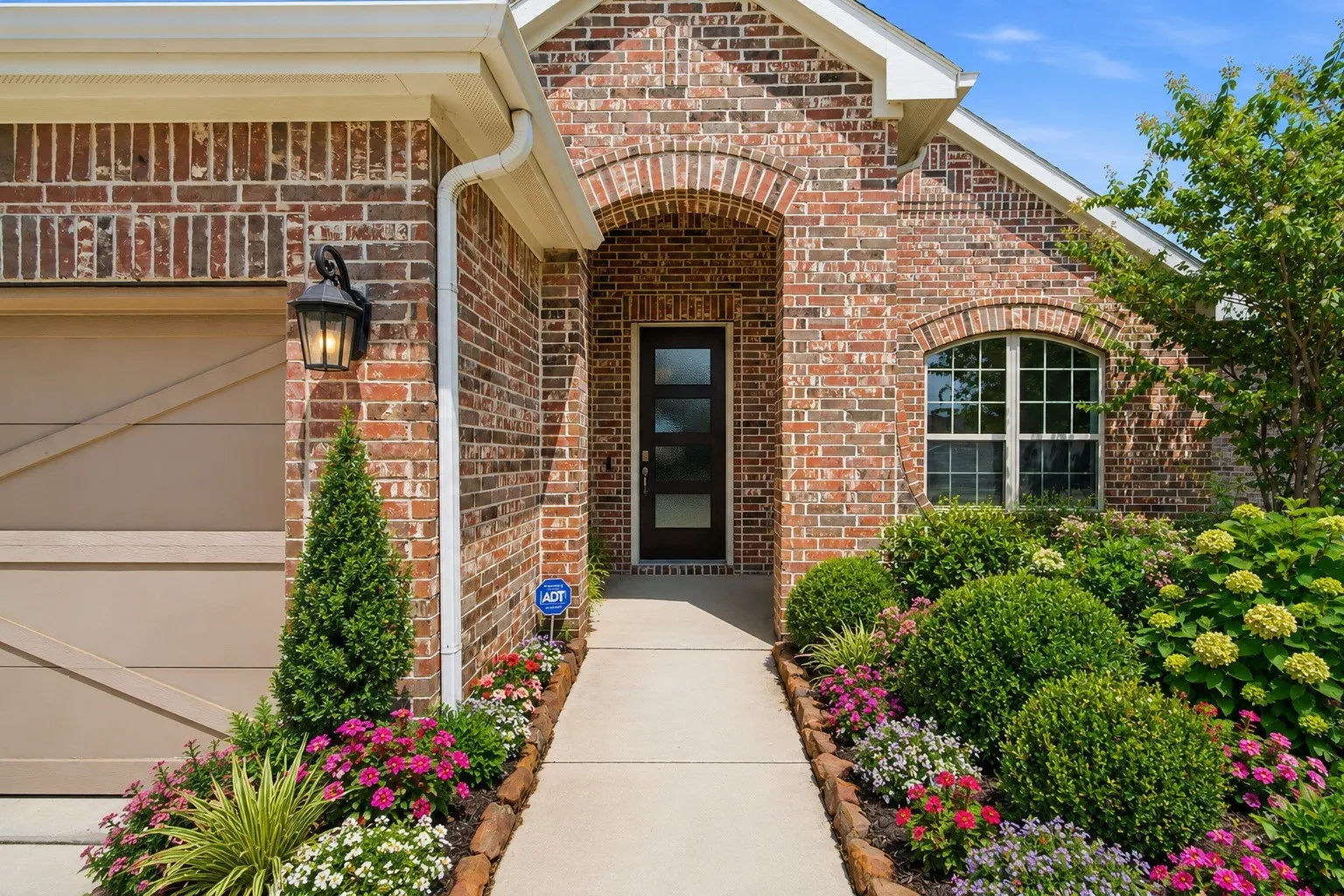 Brick exterior featuring an arched entry, a panel garage door, a front window with grid panes, and a concrete walkway (virtually landscaped)