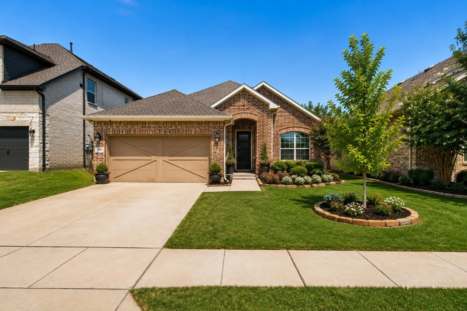 Brick facade residence featuring a two-car garage with carriage-style doors, a concrete driveway, and an arched entry