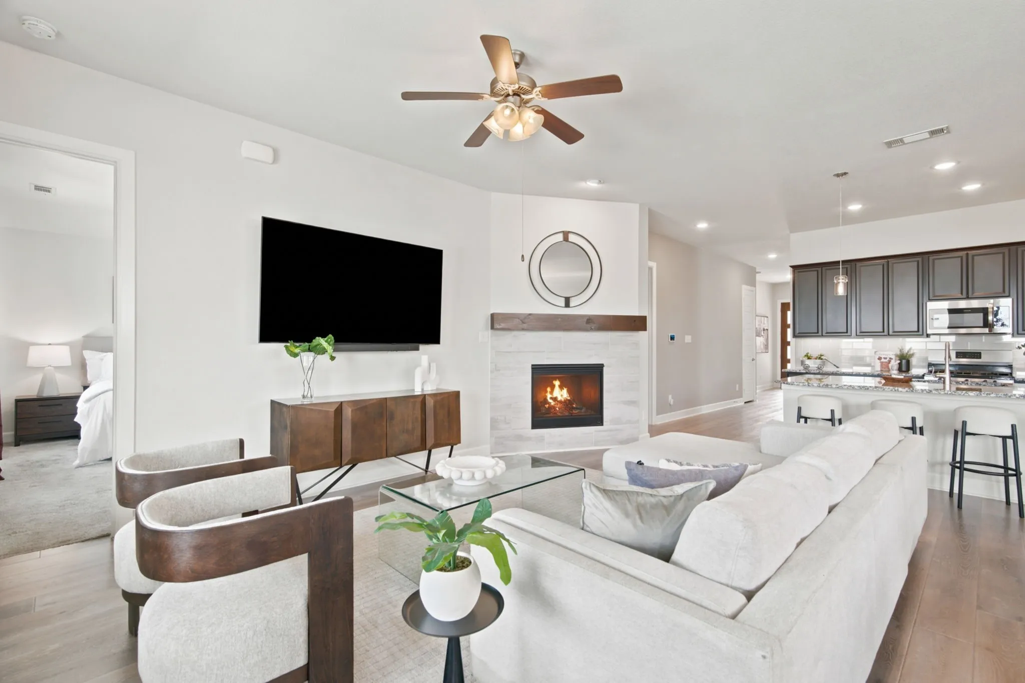 Open-concept living space featuring wood-finish flooring, a contemporary fireplace with a wood mantle, and a ceiling fan