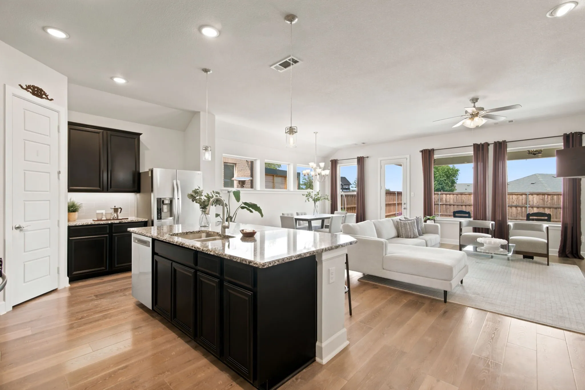 Open-concept living space featuring wood-finish flooring, recessed lighting, a kitchen island with stone countertops and an undermount sink, and black cabinetry with stainless steel appliances