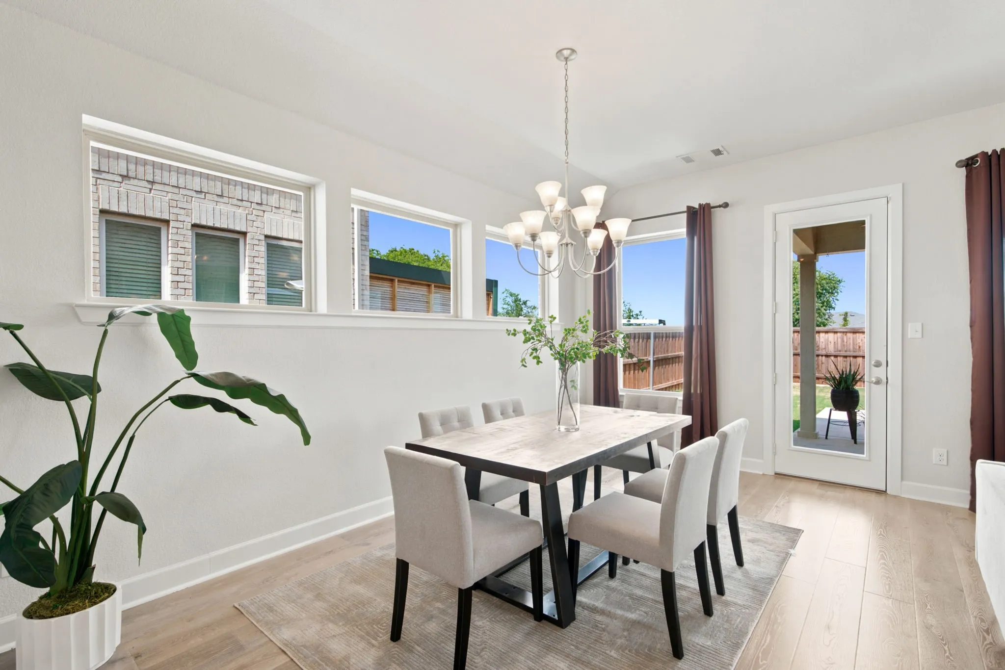 Dining area featuring wood-finish flooring, a contemporary chandelier, multiple windows, and direct access to an outdoor patio